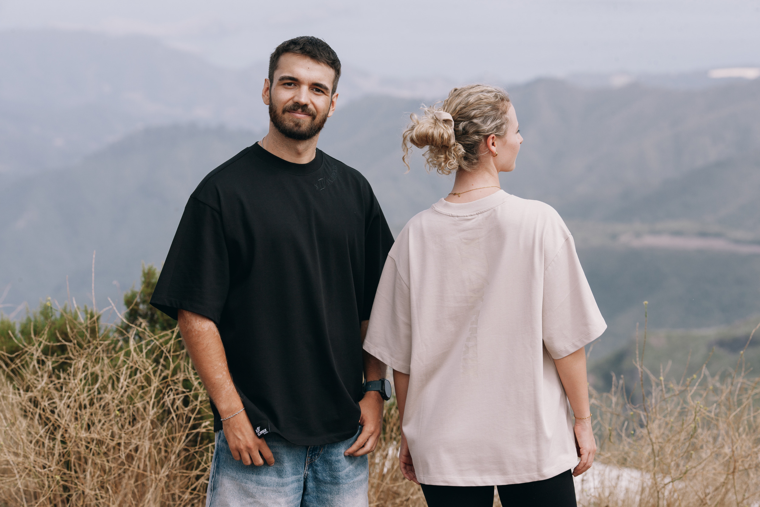 Man in black facing the camera, woman in beige seen from behind, dry grass and haze, Madeira