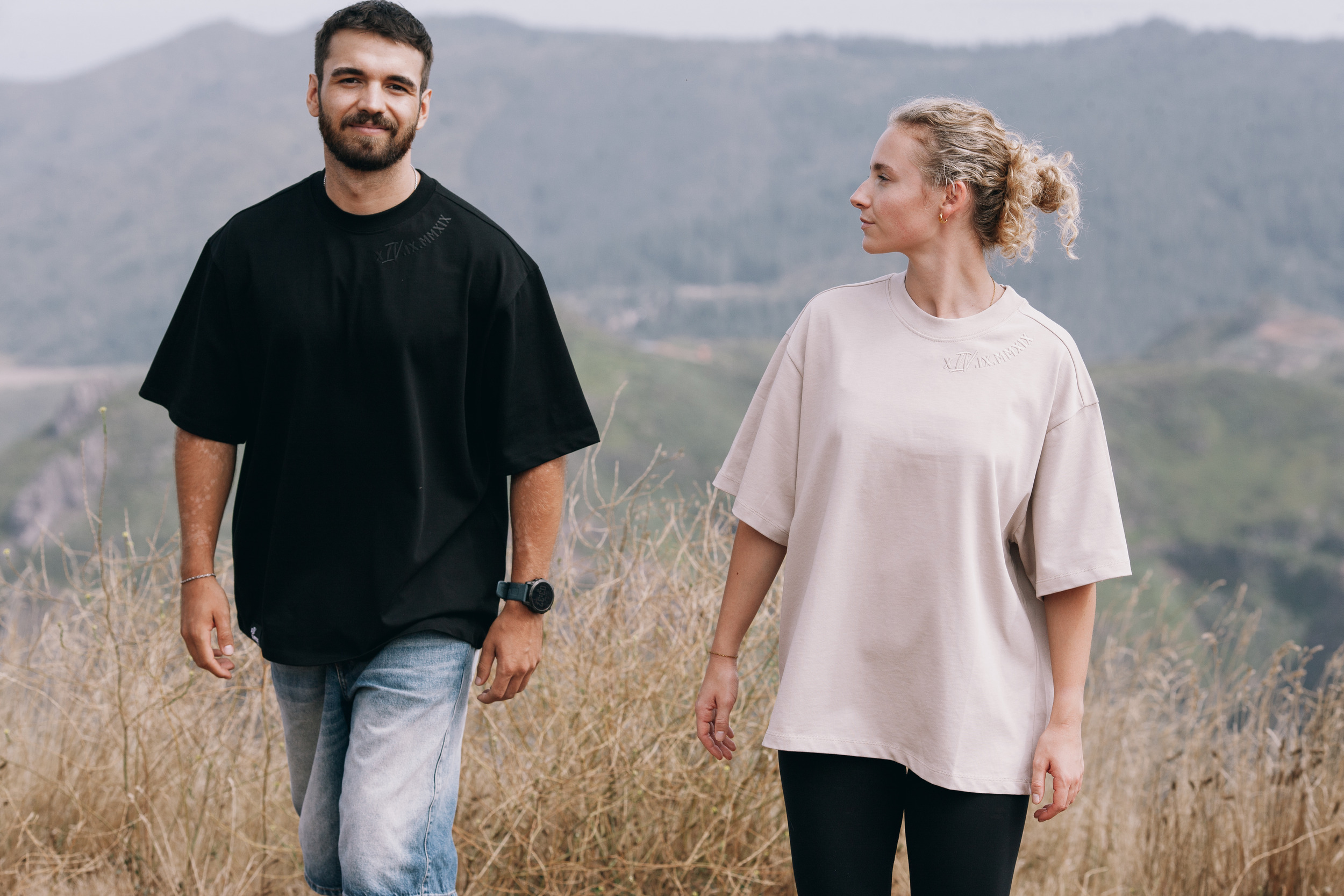 Man in an oversized black tee looking at the camera while the woman in beige looks across, Madeira