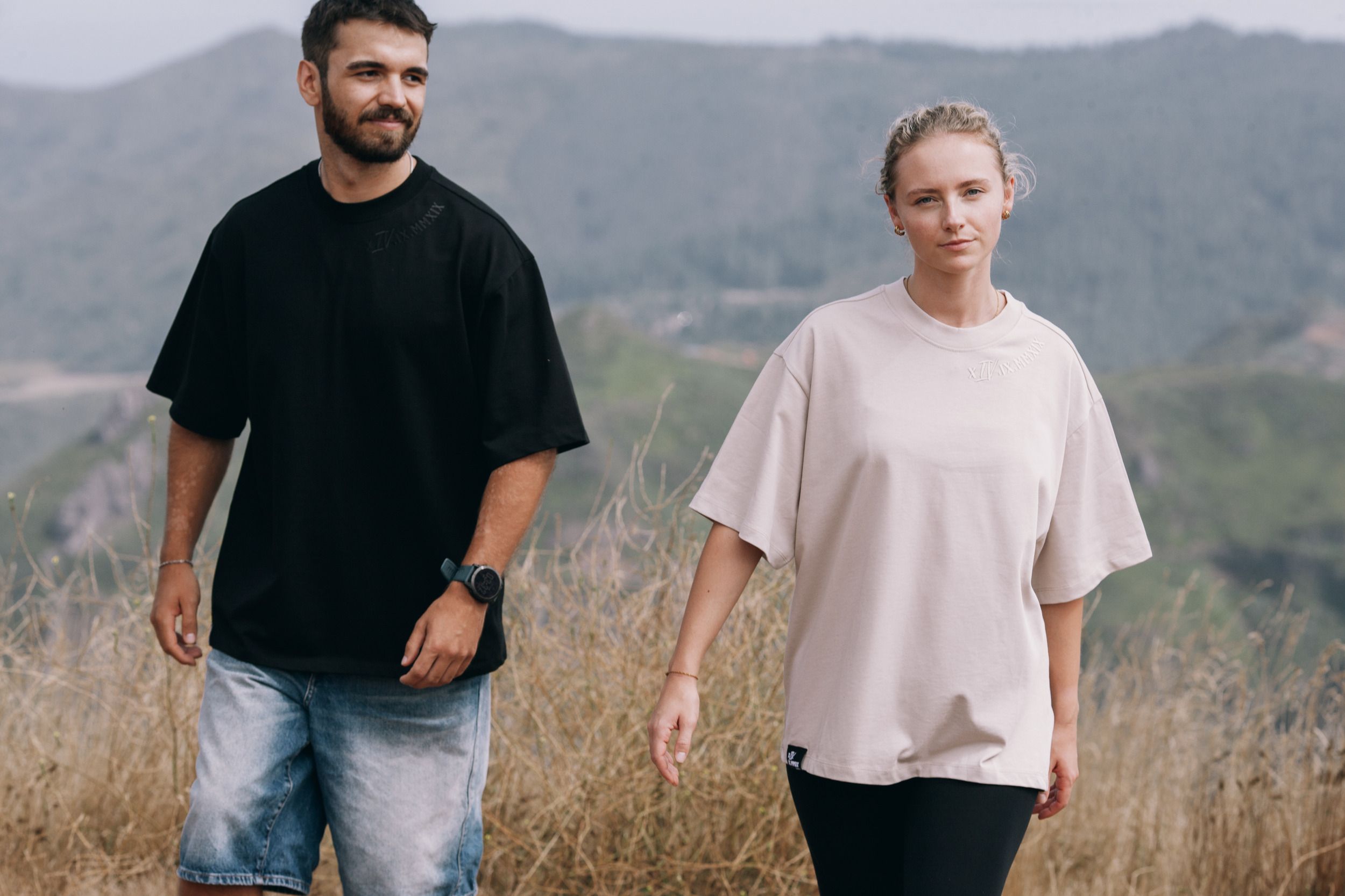 Both models walking through waist high dry grass in oversized tees, Madeira highlands