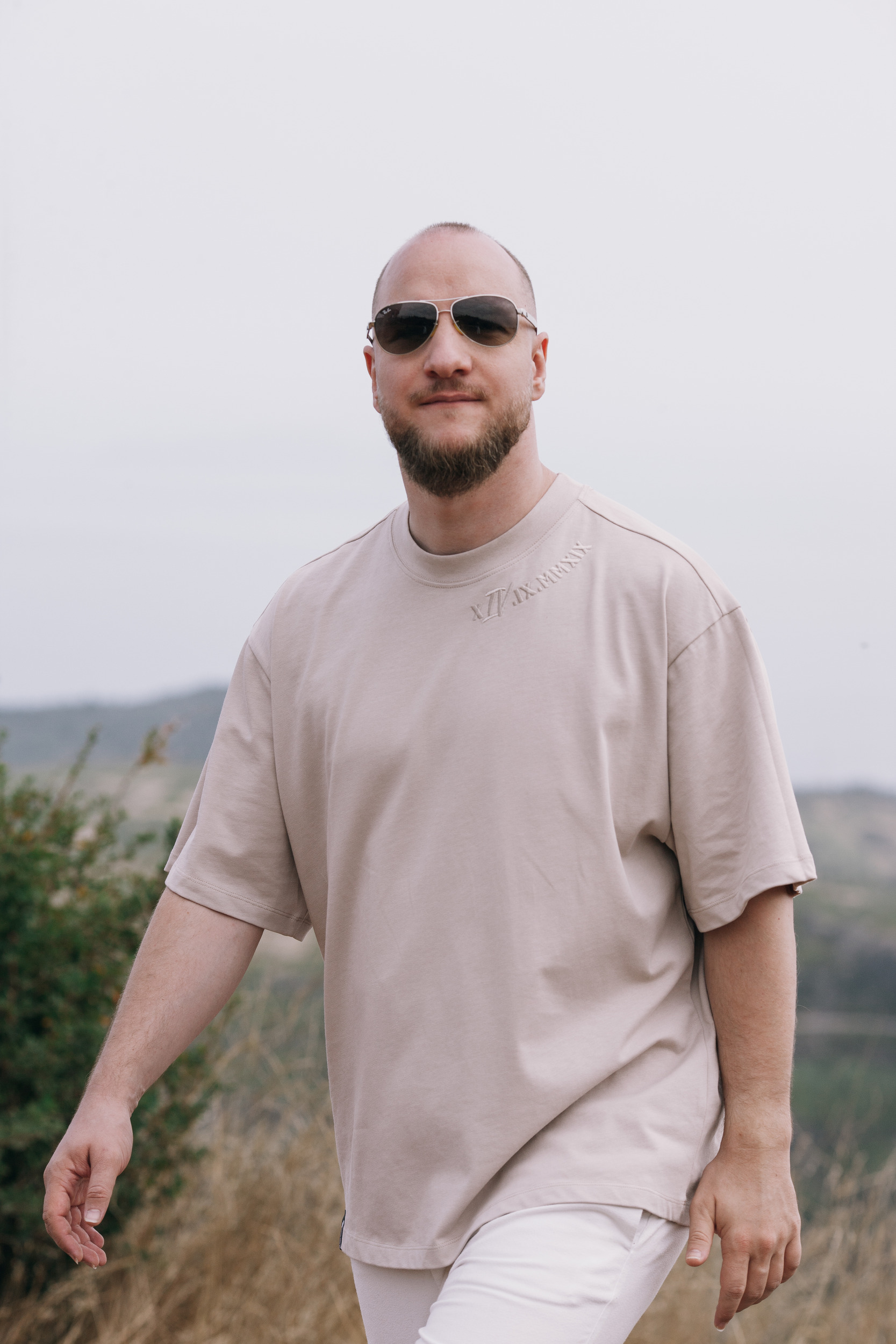 Man walking in the beige oversized tee, dry scrub and haze behind, Madeira highlands