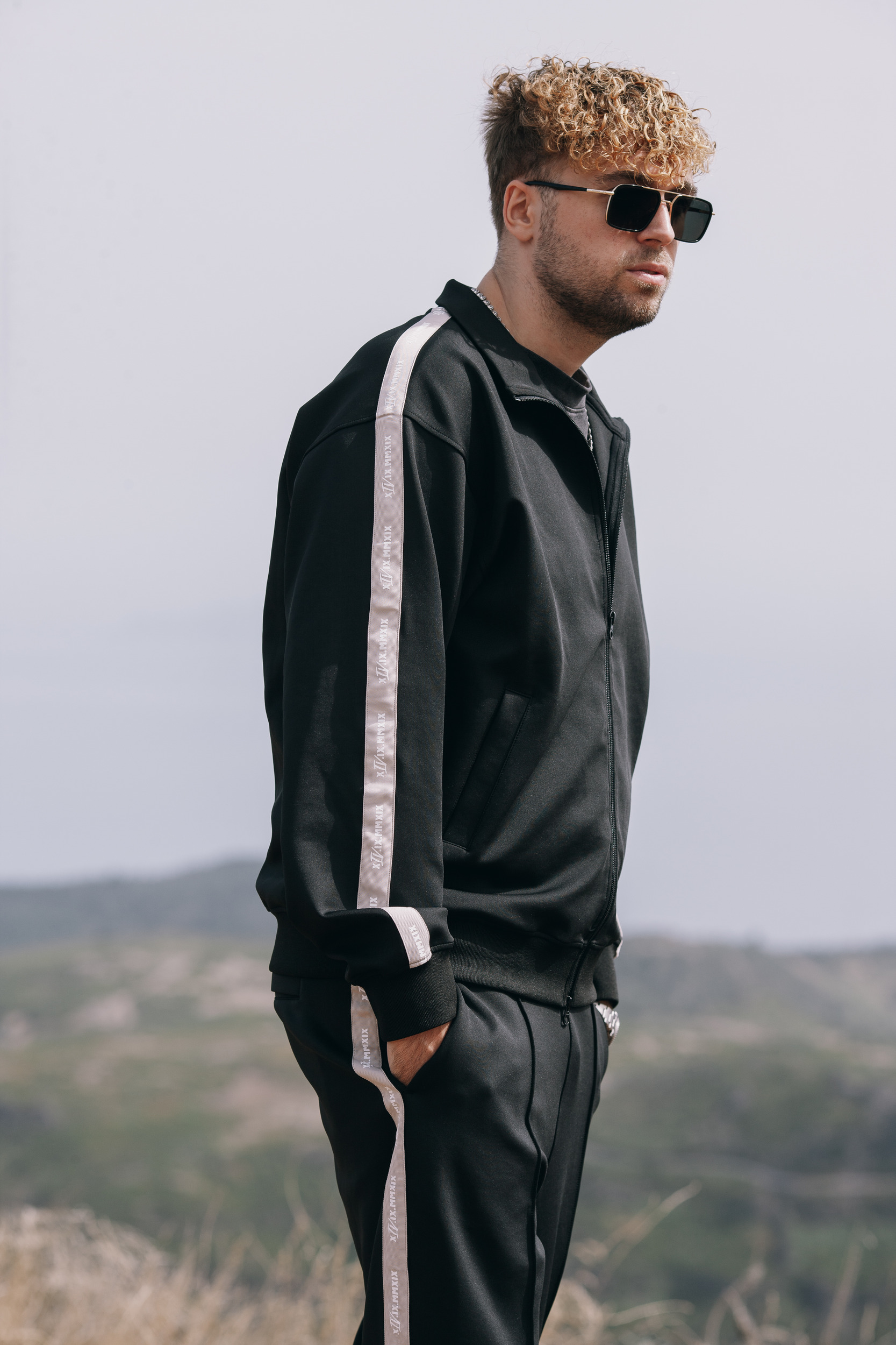Man in the black track jacket standing with hands in pockets, hazy ridges behind, Madeira