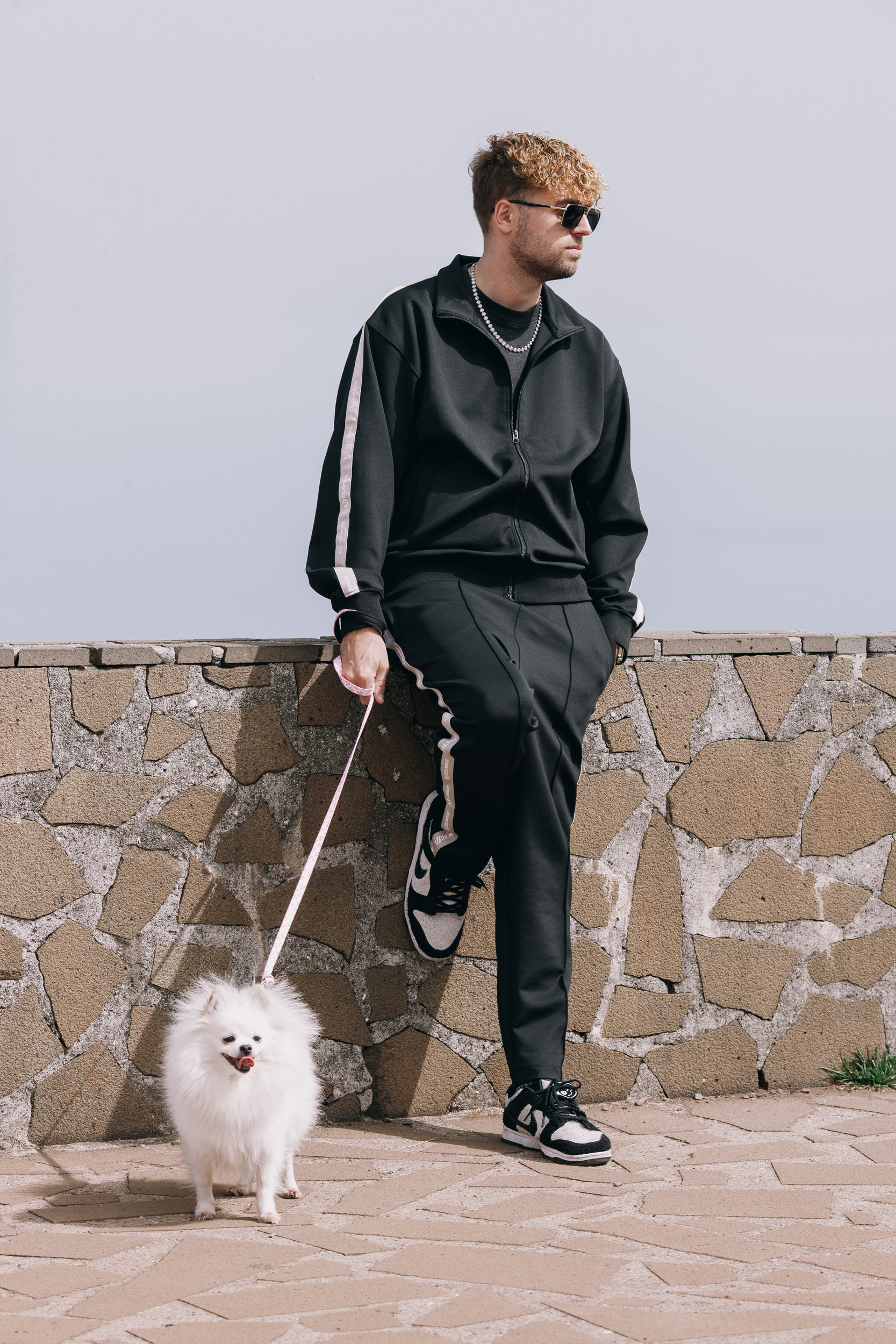 Man sitting on a stone viewpoint wall with a small white pomeranian on a lead, Madeira highlands