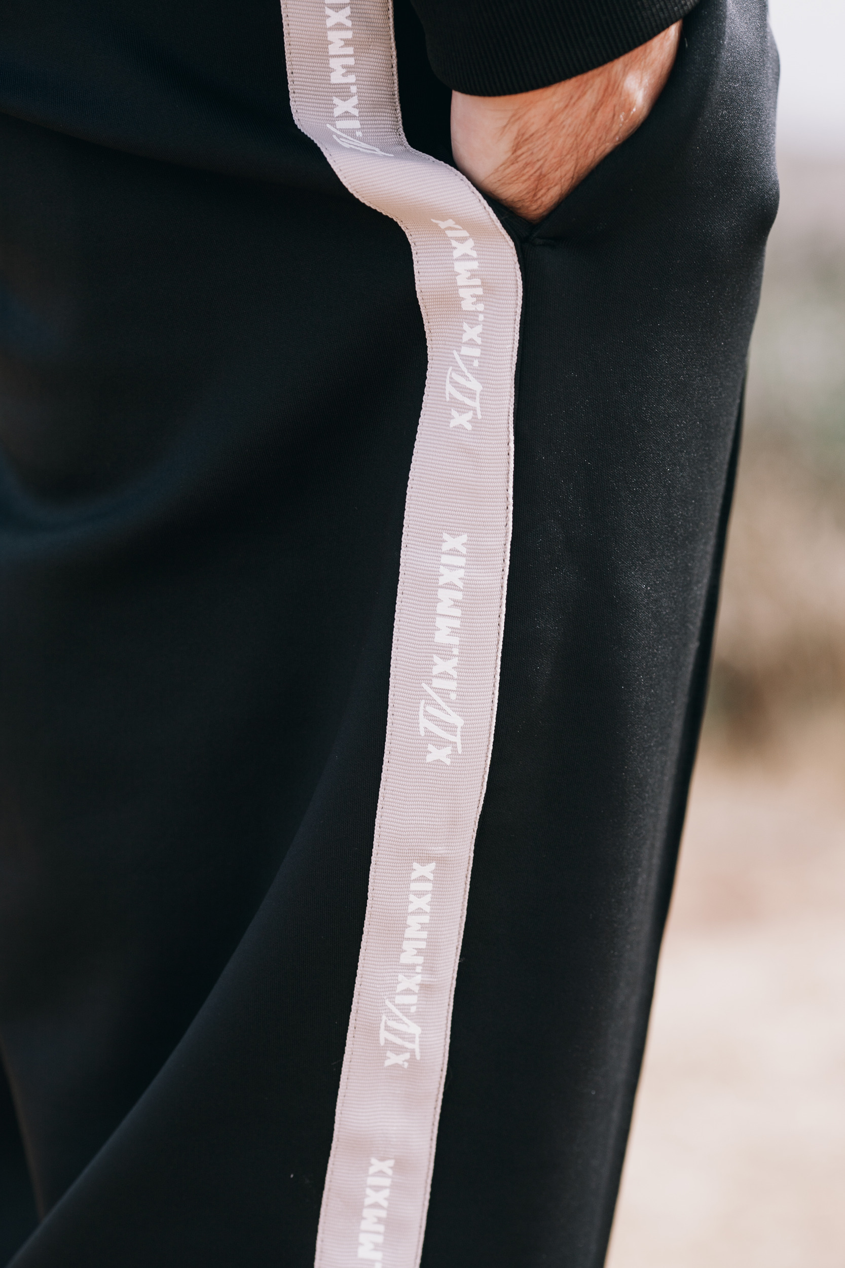 Side stripe of the track pants with a hand in the pocket, close detail