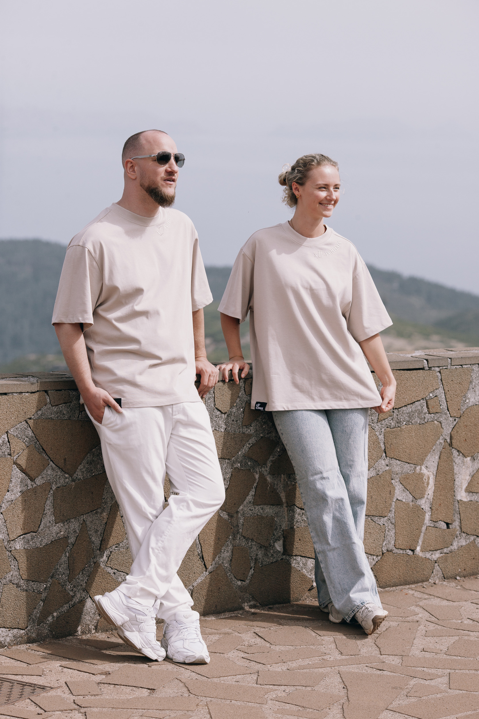 Two models in beige leaning against the stone viewpoint wall, Madeira highlands