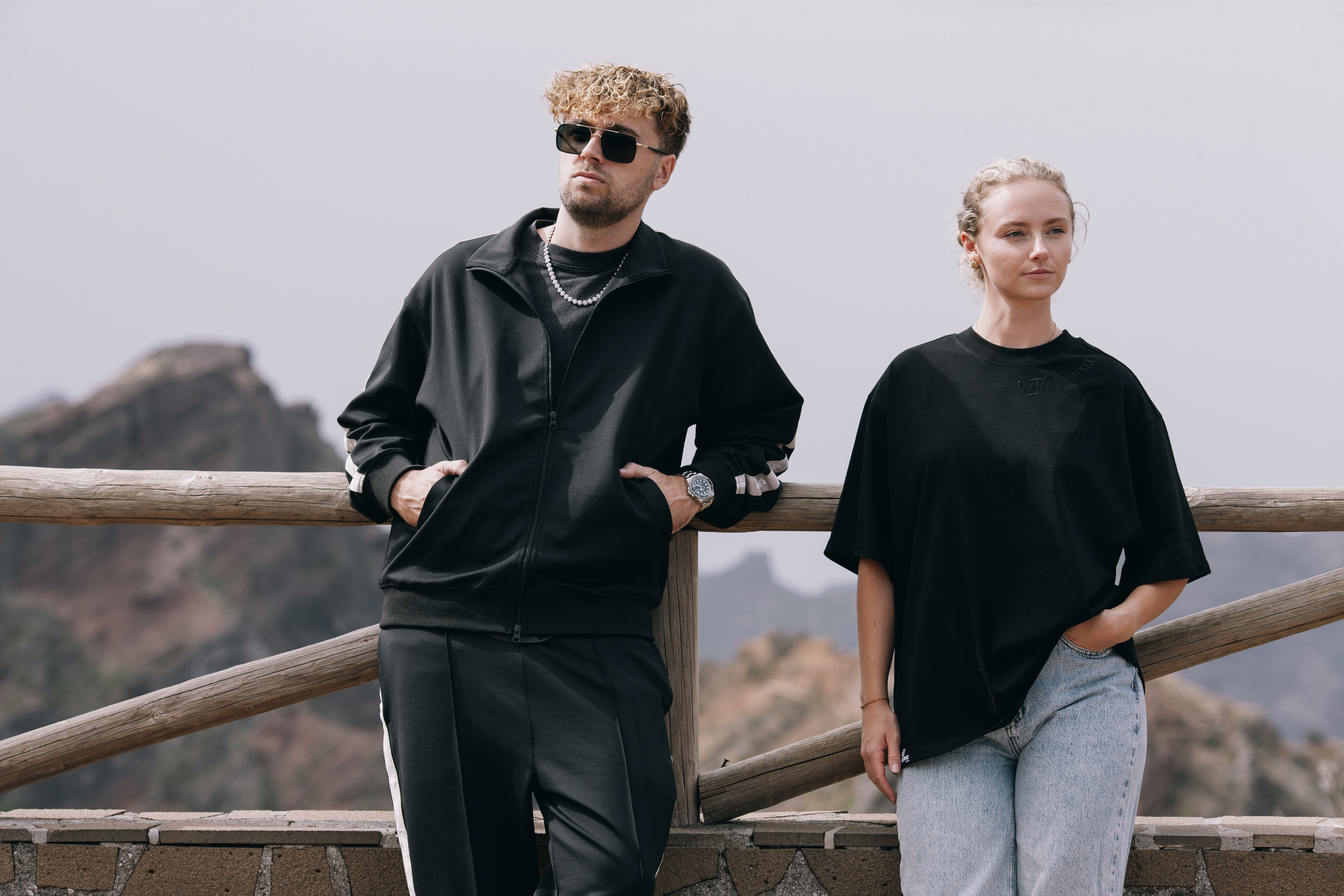 Man leaning back on the wooden railing in the black track jacket, woman beside him, Madeira