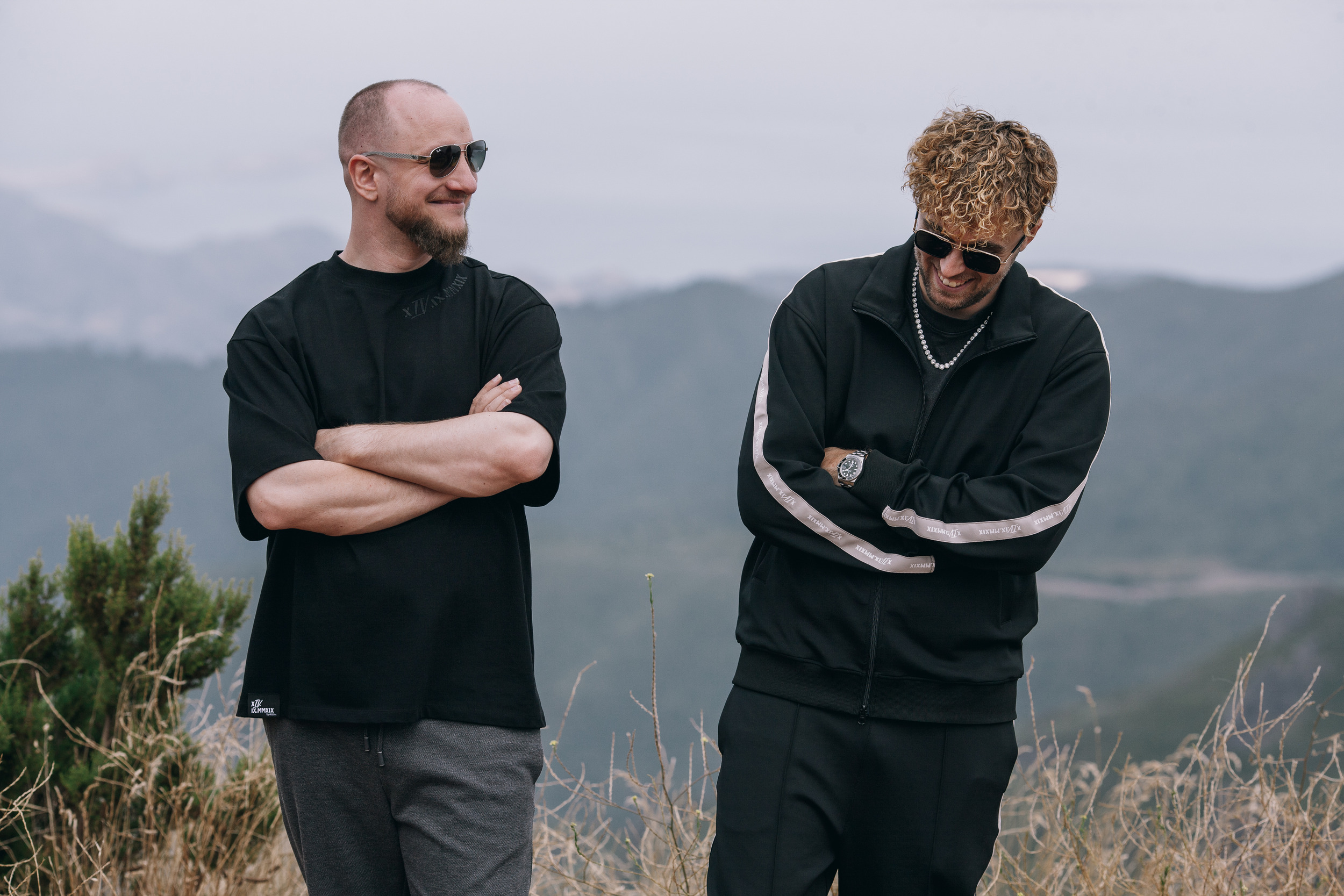 Two men standing together, one with arms crossed, hazy mountains behind, Madeira
