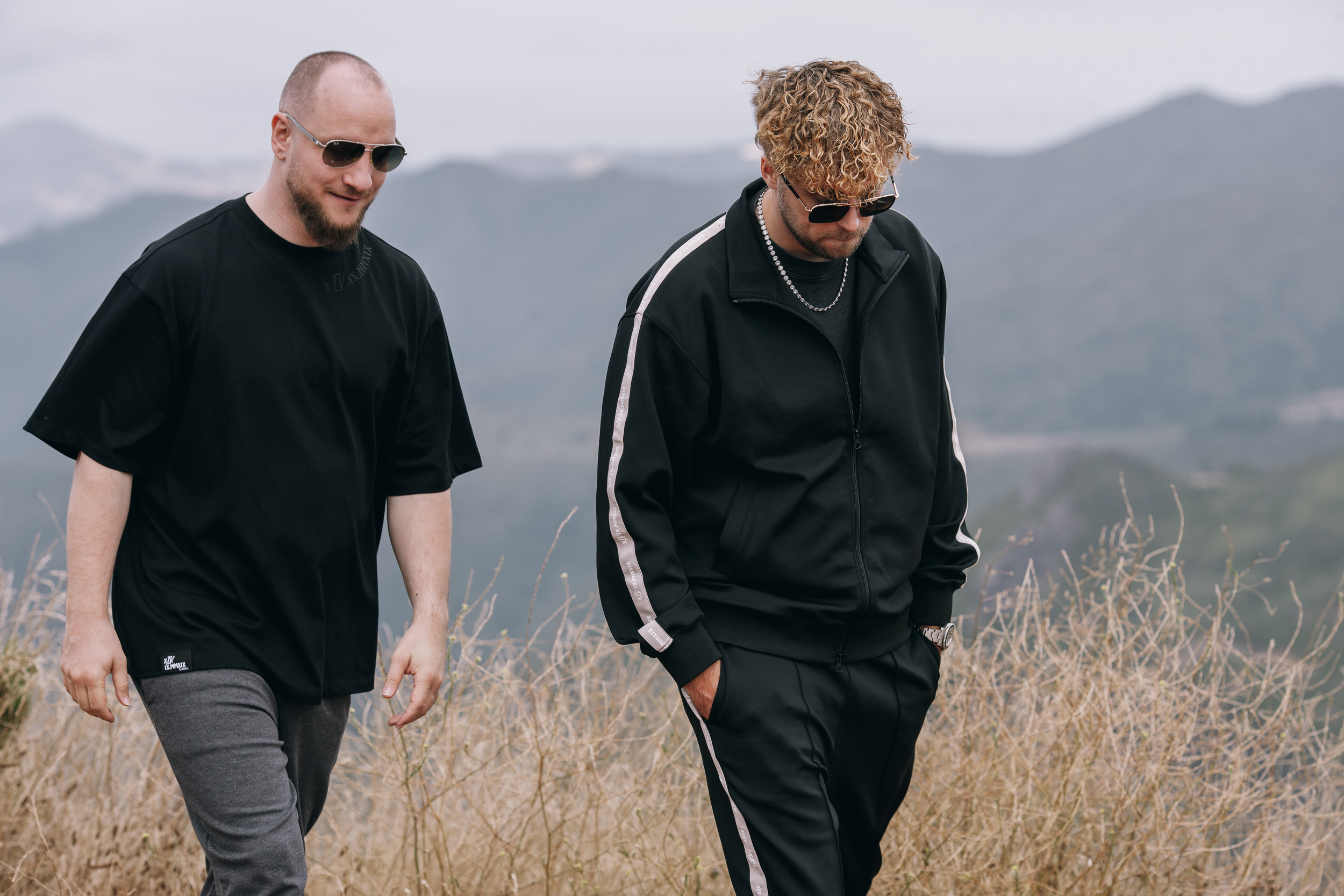 Two men walking down the slope in black, dry grass at knee height, Madeira
