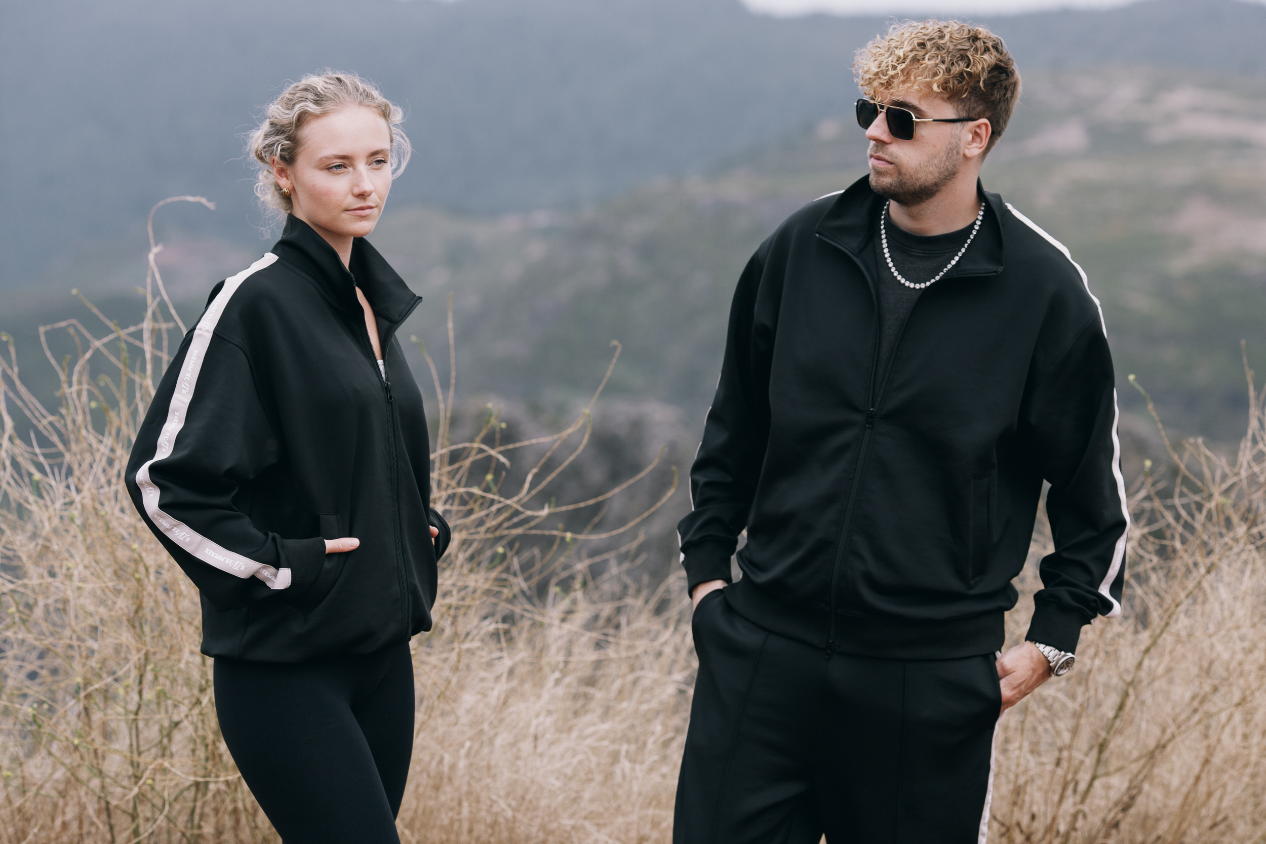 Woman and man in matching black track jackets standing in dry grass, Madeira highlands