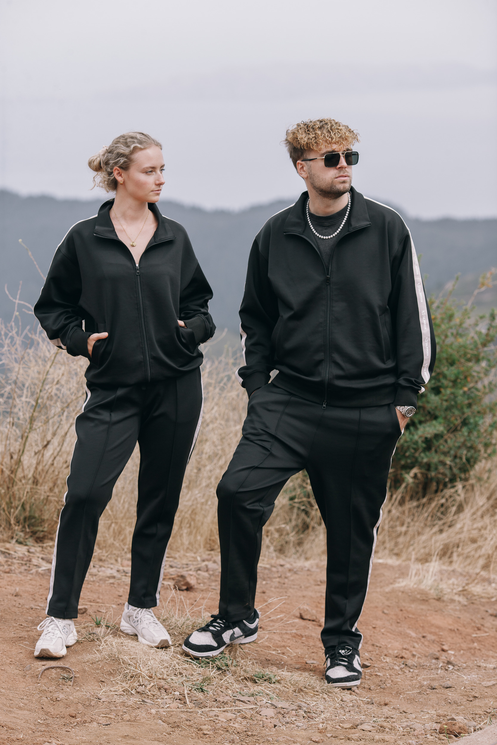 Pair standing on the slope in track suits, dry grass around them, Madeira highlands