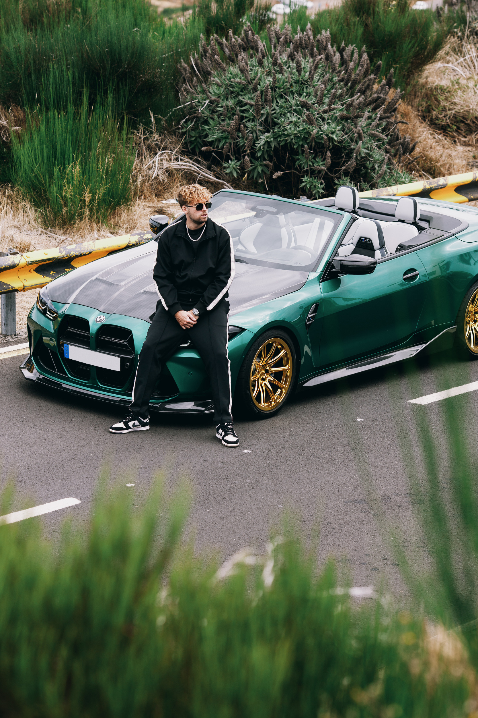 Model on the bonnet of the green convertible seen through roadside grass, Madeira