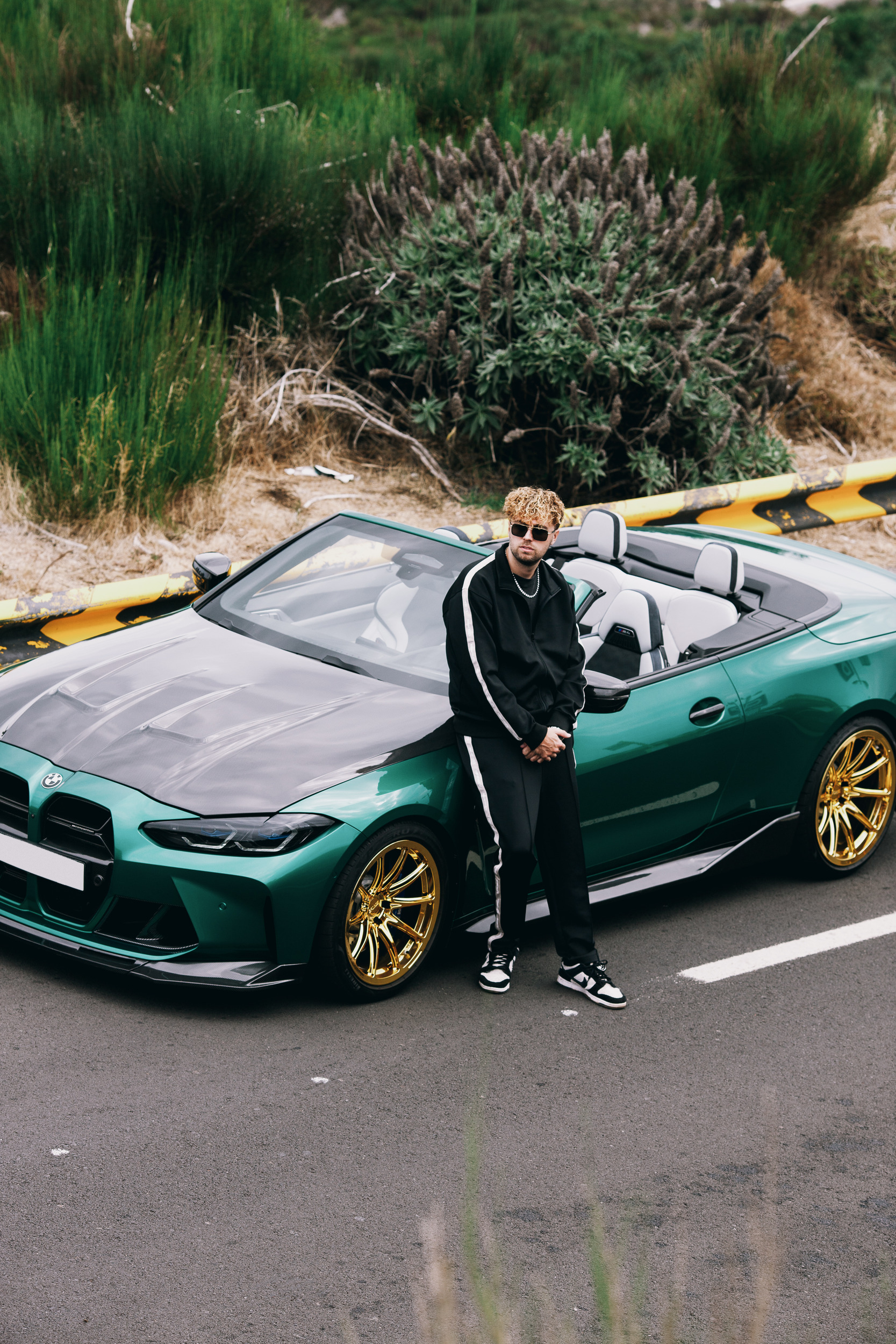 Model leaning on the door of the green convertible on the mountain road, Madeira