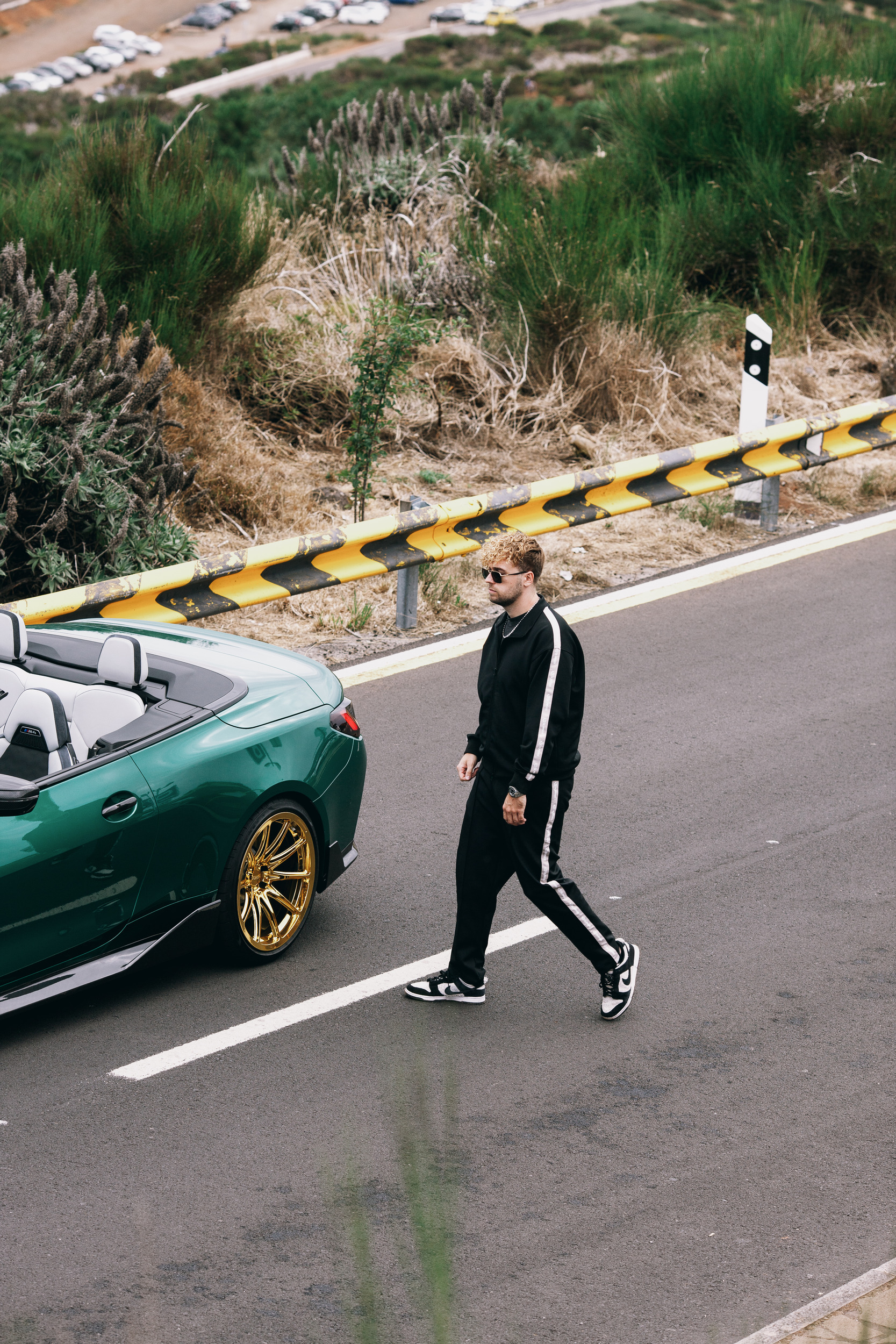 Model walking past the green convertible on the empty road, Madeira