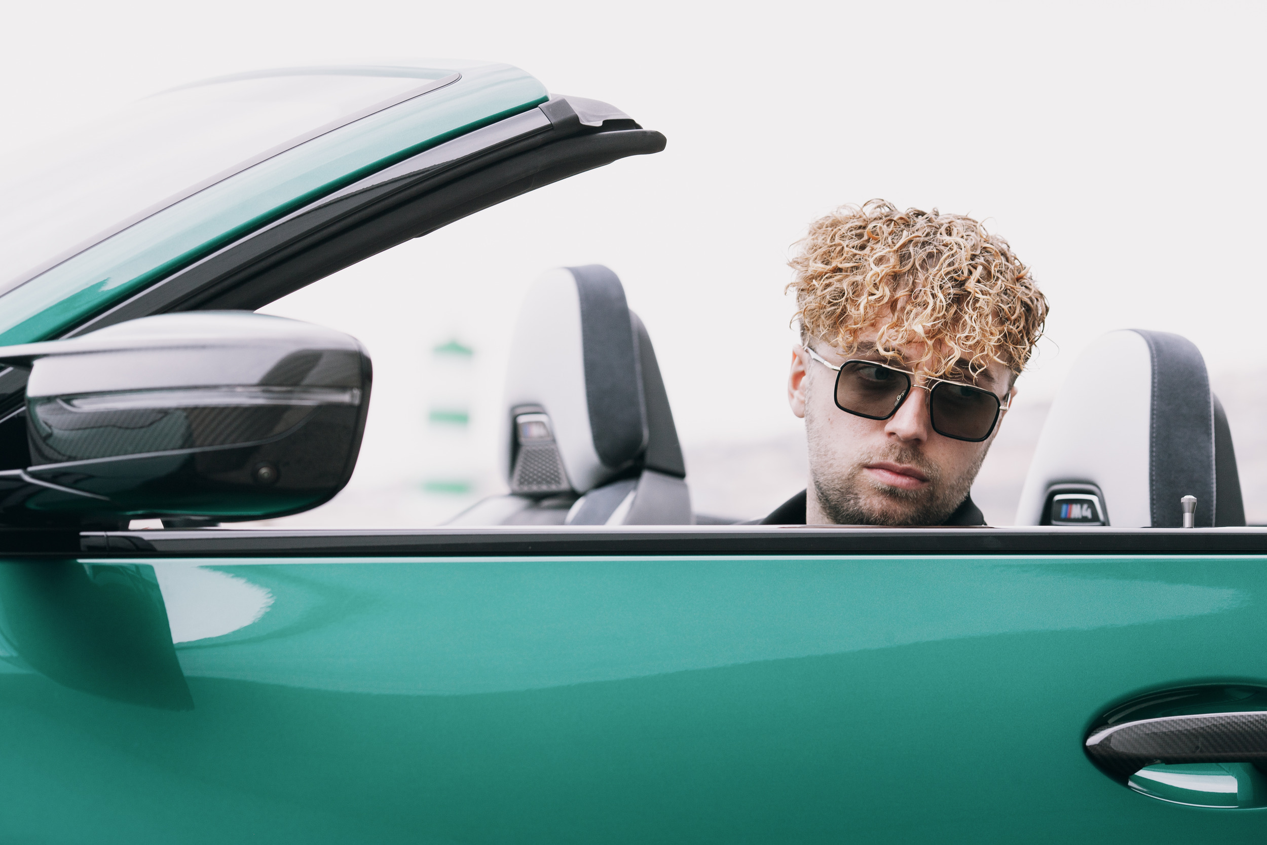 Close frame of the model in the open convertible, striped lighthouse behind, Madeira