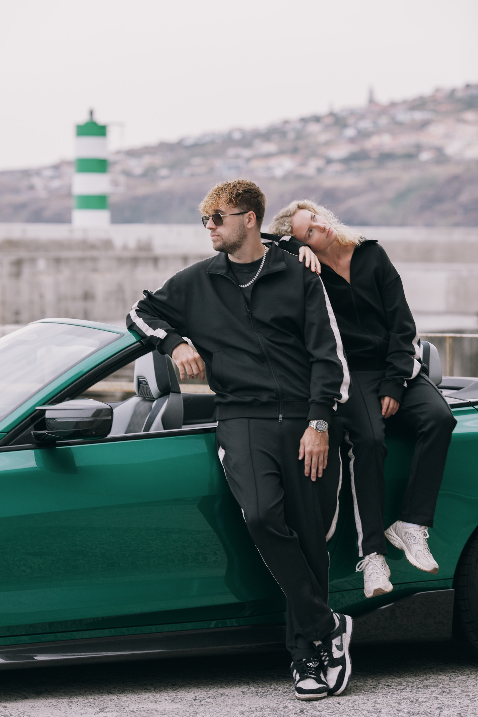 Two models leaning on the convertible, striped lighthouse tower behind, Madeira
