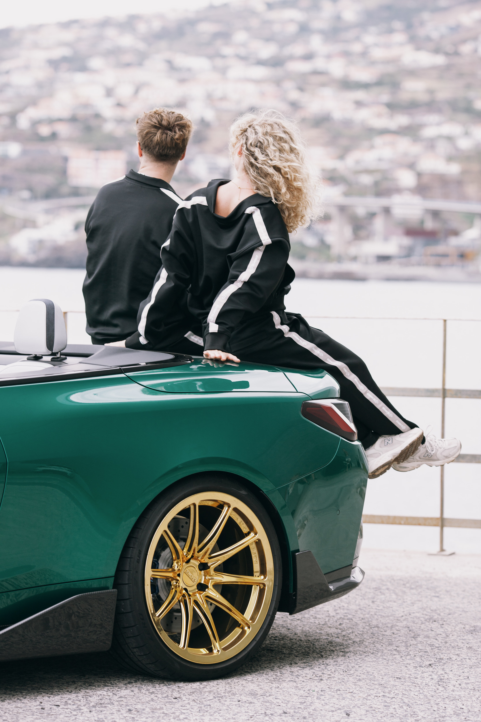 Two models sitting on the boot of the green convertible, gold wheels below, Madeira
