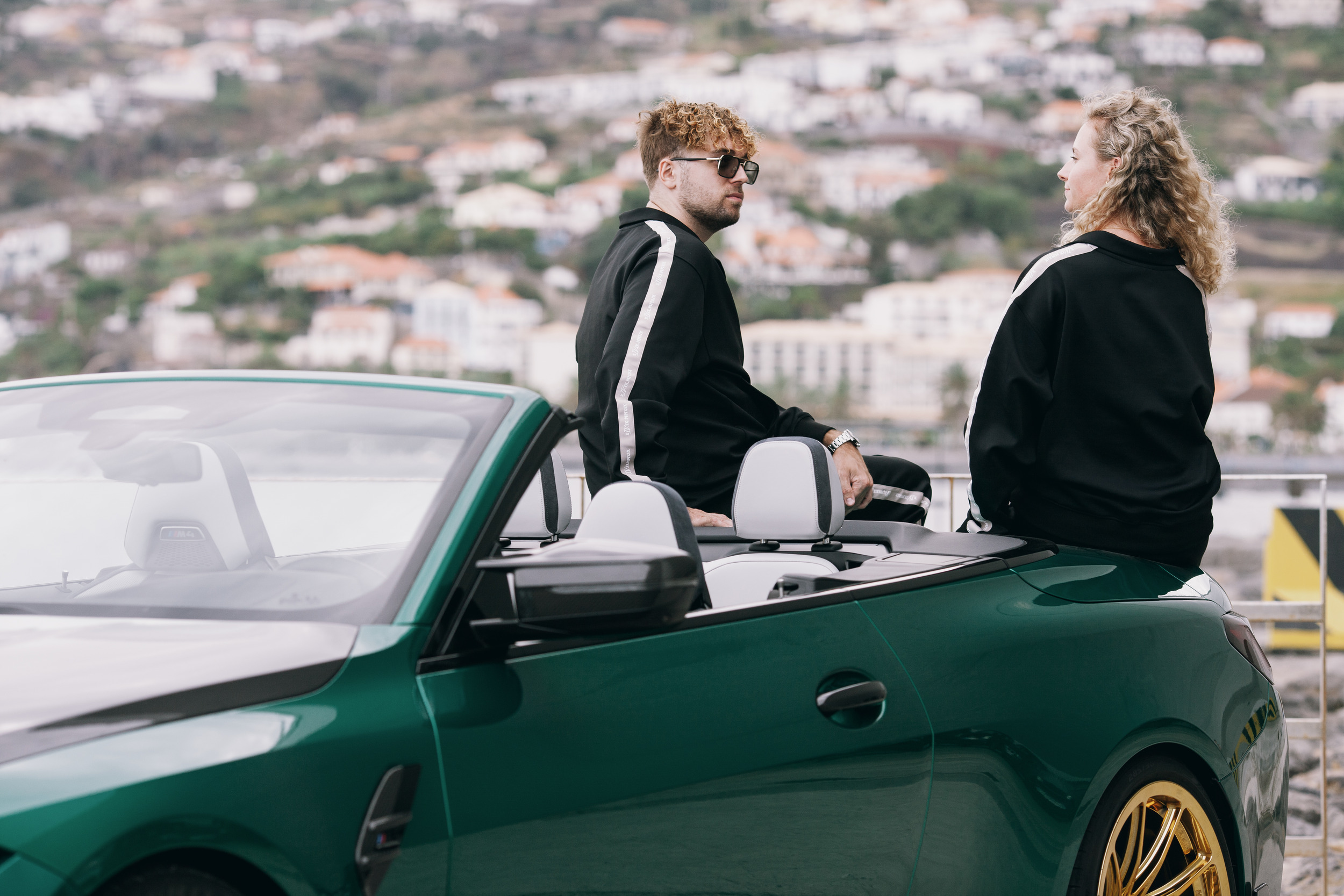 Model sitting on the seat back of the open car while the woman stands beside it, Madeira