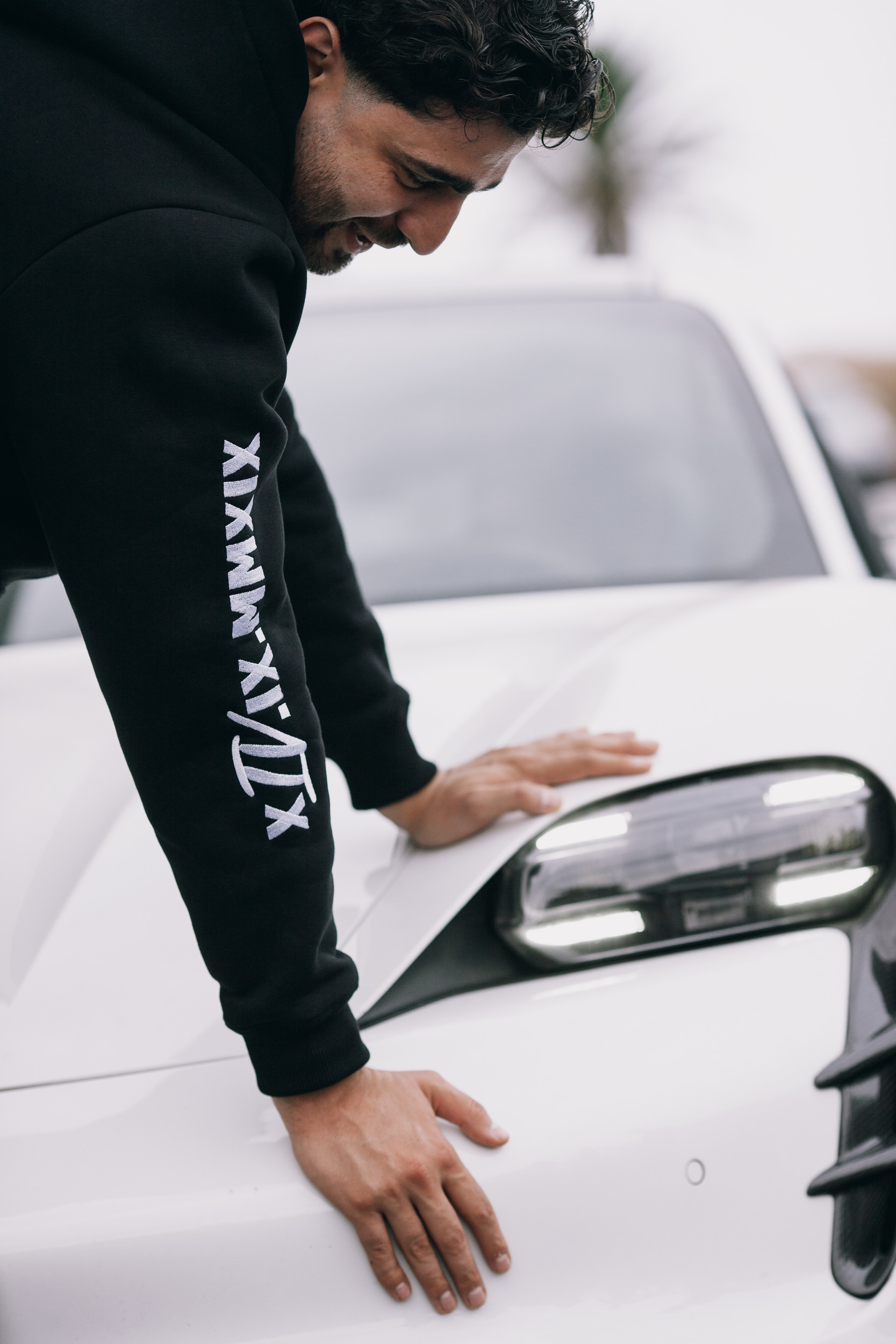 Hand resting on the bonnet of the white car, hoodie sleeve print in frame, Madeira