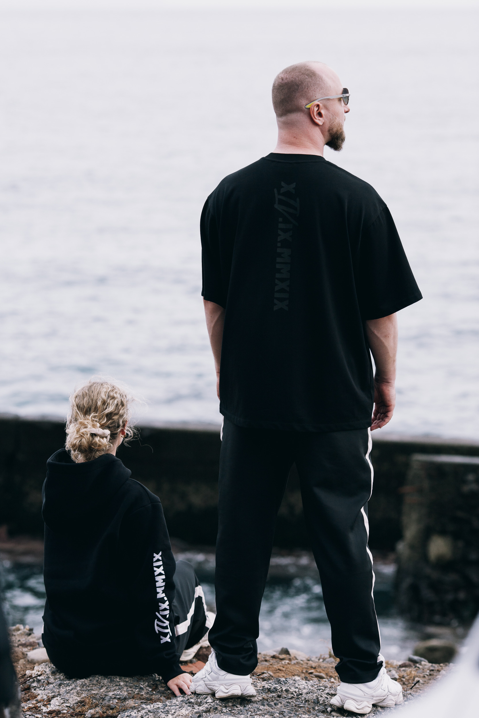 Man seen from behind at the sea wall while another model sits below, Madeira