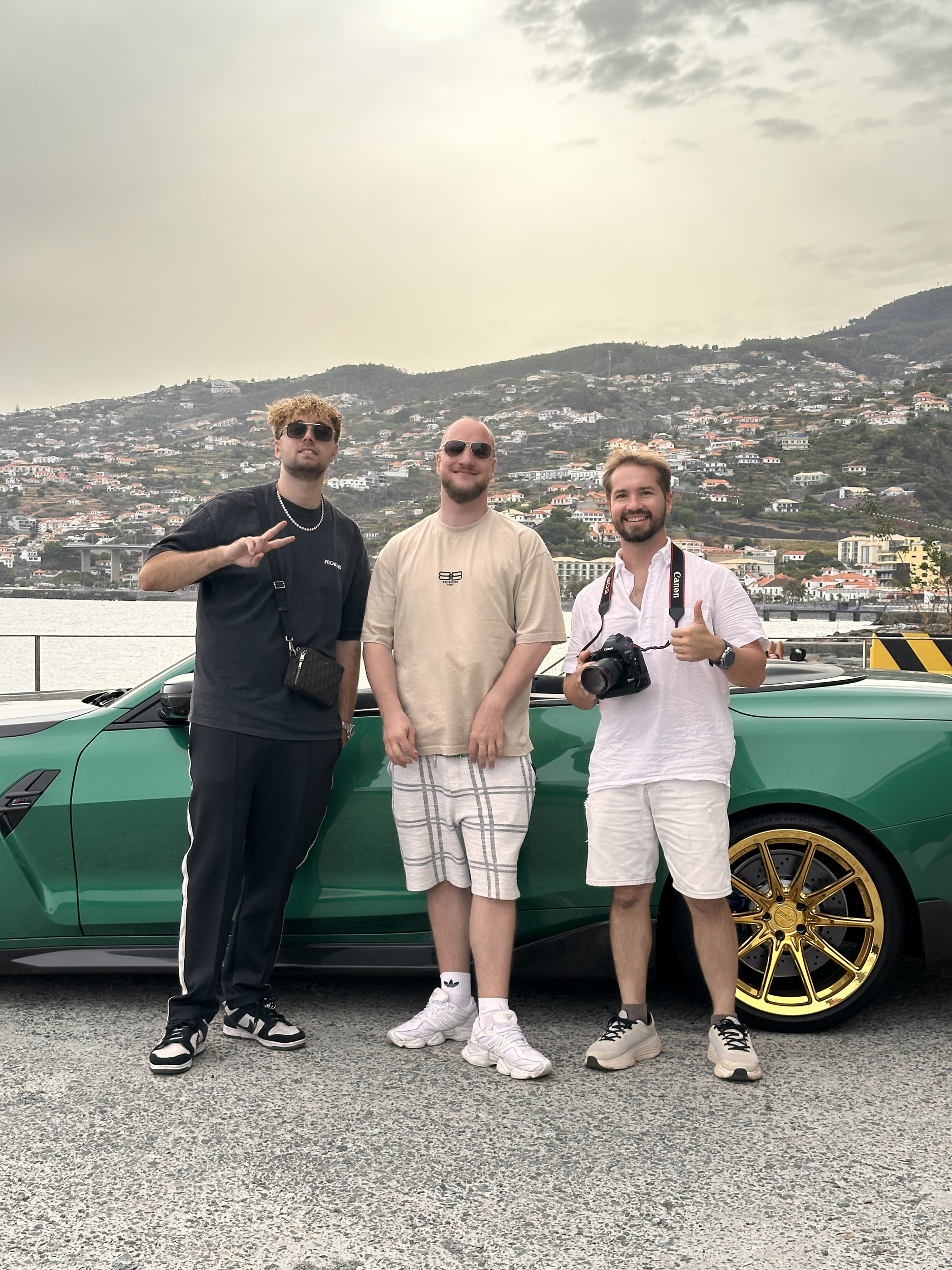 Group photograph beside the green convertible, hillside town and harbour behind, end of the shooting day, Madeira