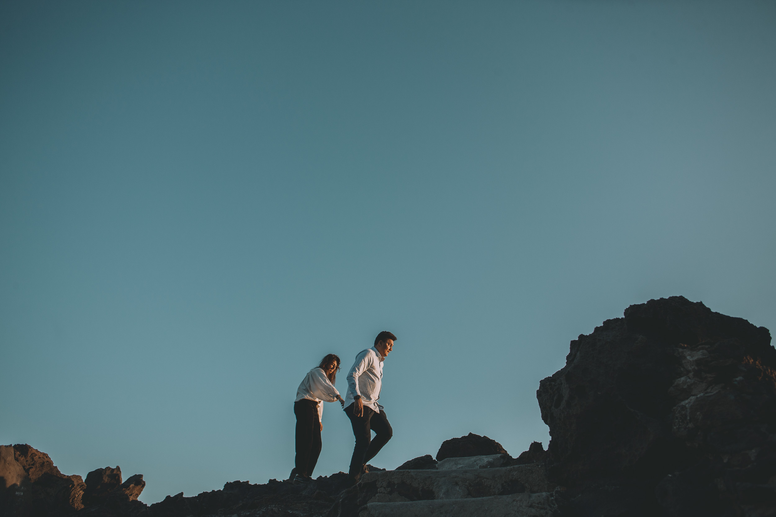 Couple small against a vast deep blue sky, walking along volcanic rock formations at Praia Formosa, Madeira
