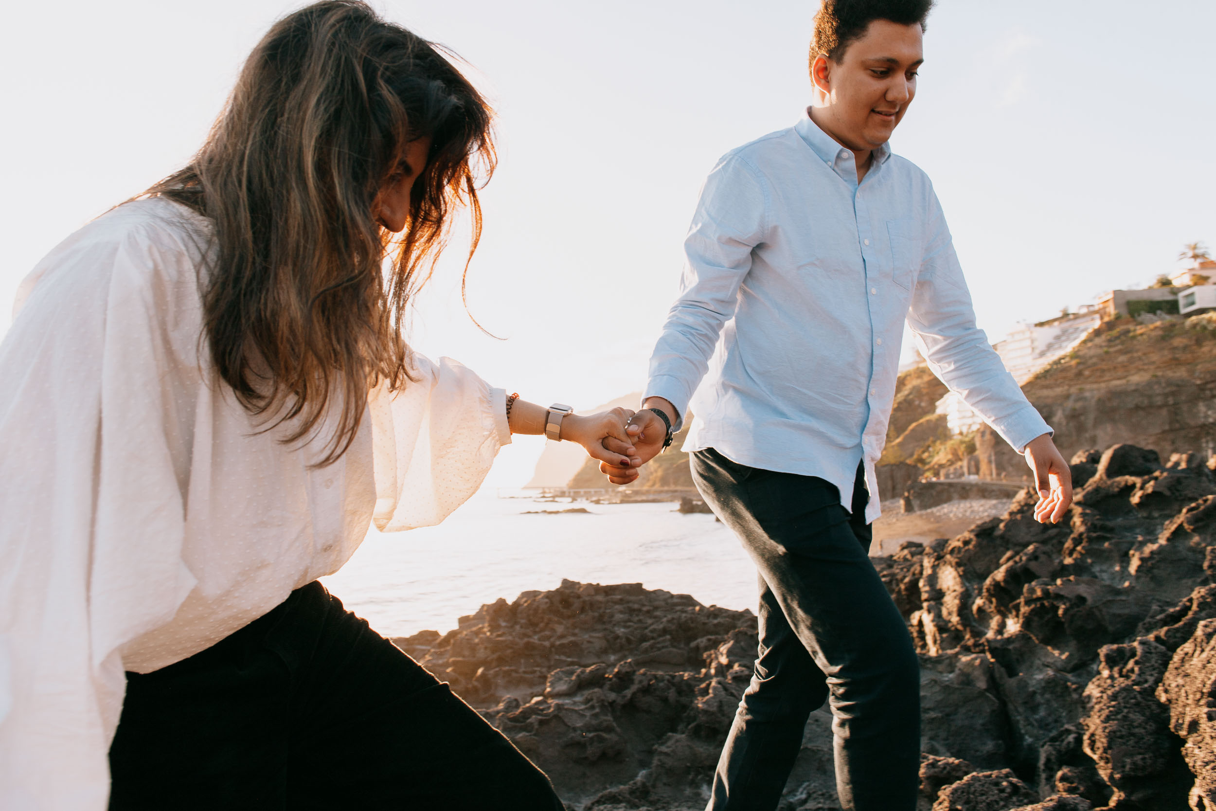 Couple walking hand in hand on pebble beach at Praia Formosa, backs to camera, warm sunset light, Funchal, Madeira