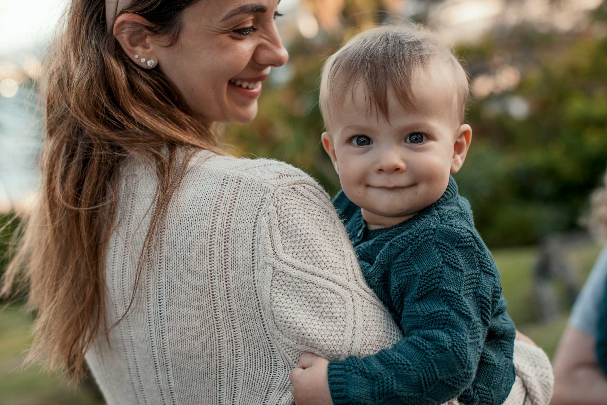 Close-up of mother smiling down at baby in her arms, baby looking directly at camera with a gentle expression, Santa Catarina Park, Madeira