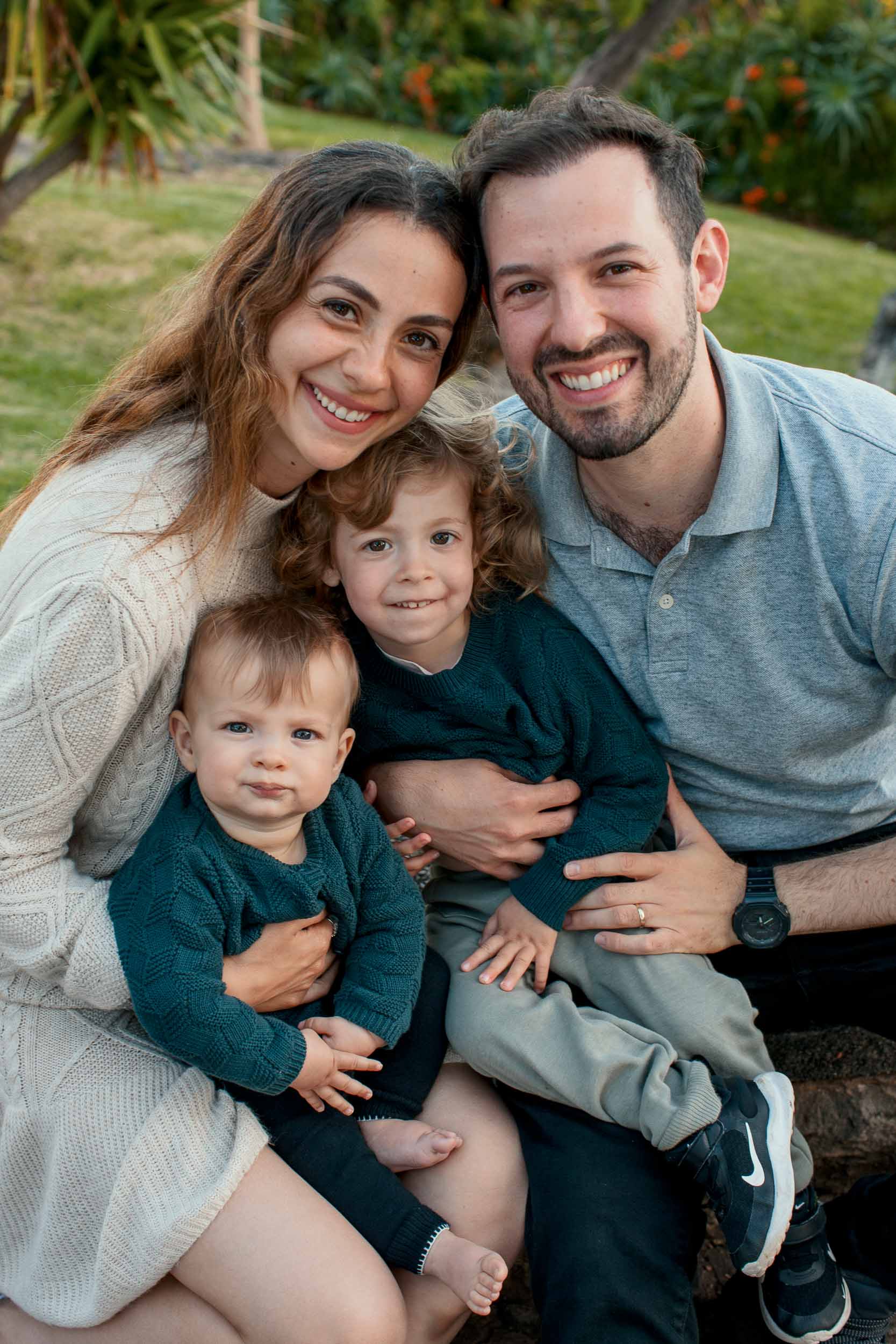 Portrait of family of four seated together, both parents and children smiling, park greenery behind, Santa Catarina Park, Funchal, Madeira