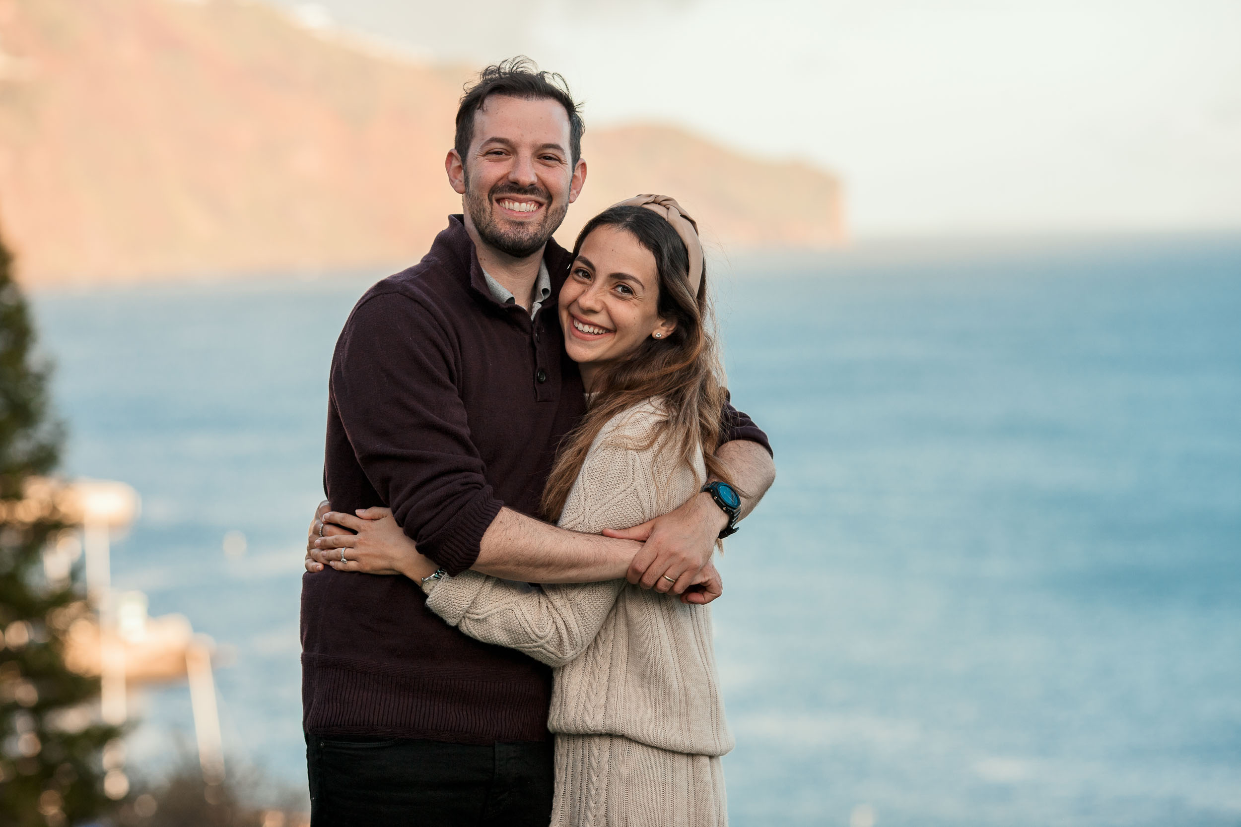 Parents embracing at Santa Catarina Park, Atlantic ocean and Funchal cliffs in the background, warm late afternoon light, Madeira