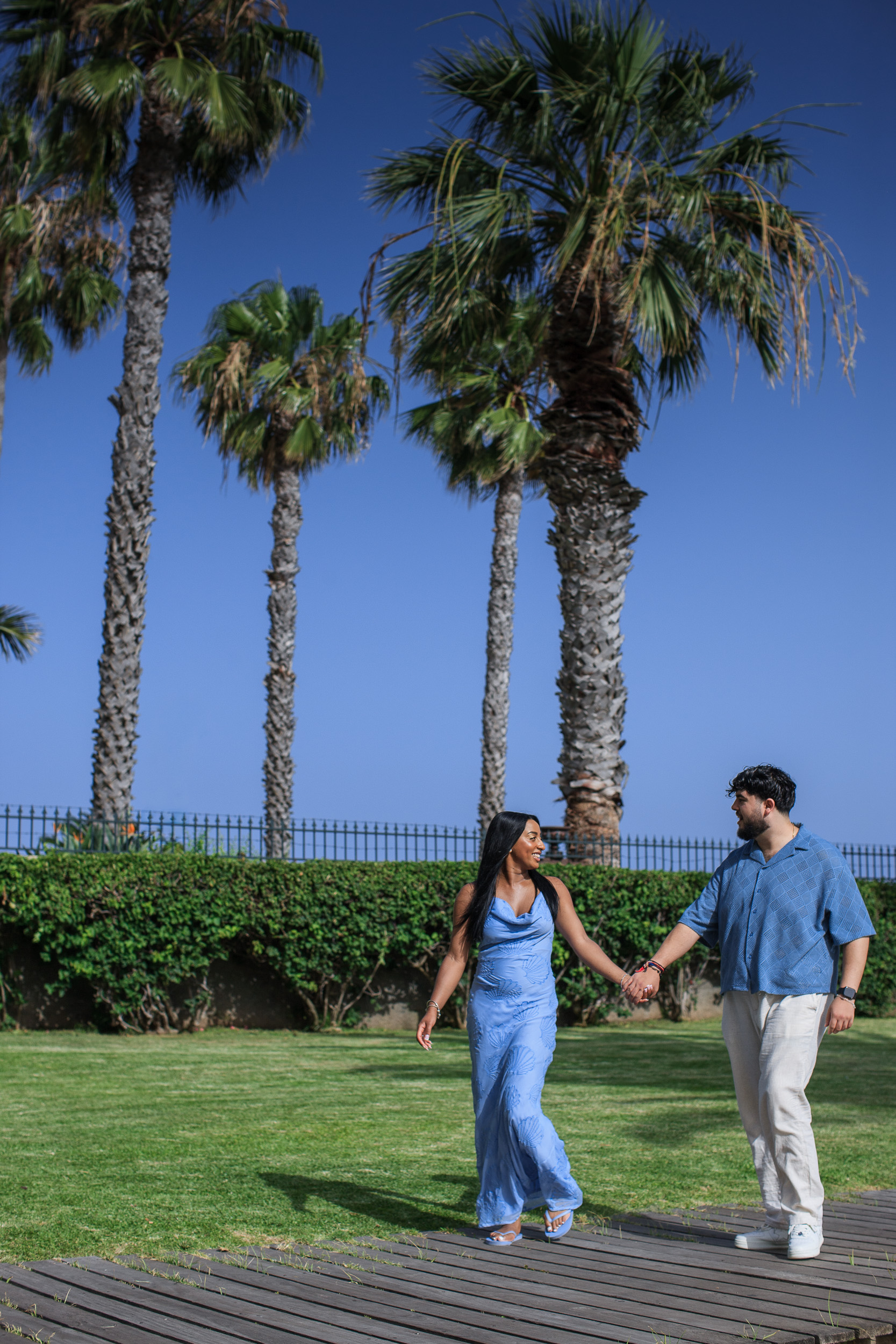 Walking hand in hand across the boardwalk under the palms, central Funchal, Madeira