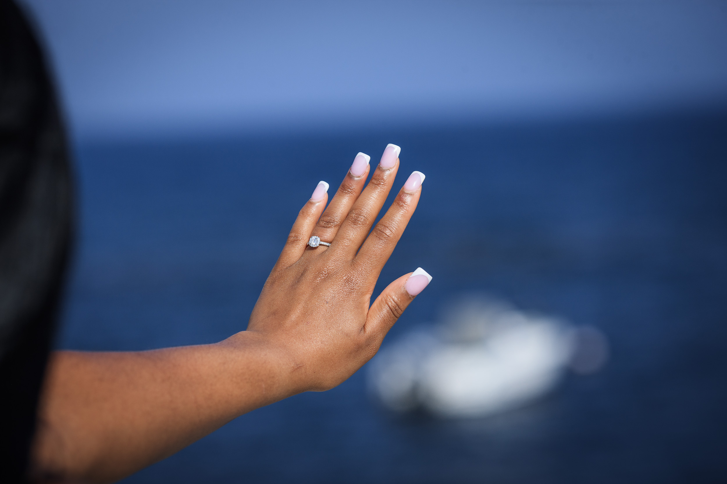 Her hand with the engagement ring raised against the Atlantic and a white boat, Madeira