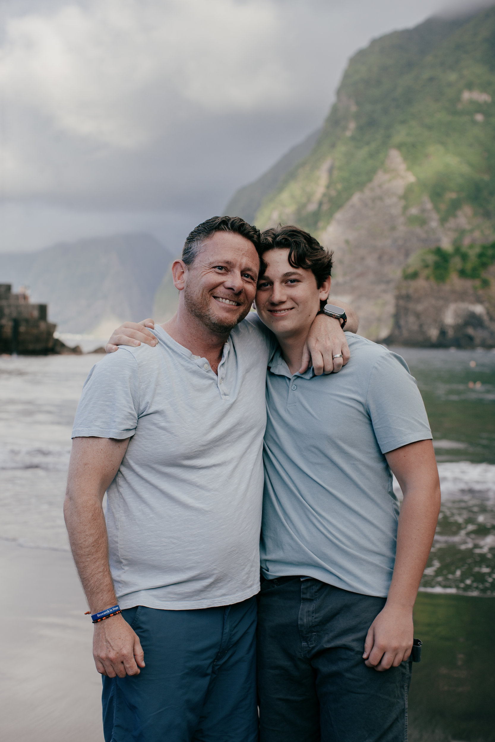 Father and teenage son hugging on the shore at Seixal, north coast of Madeira
