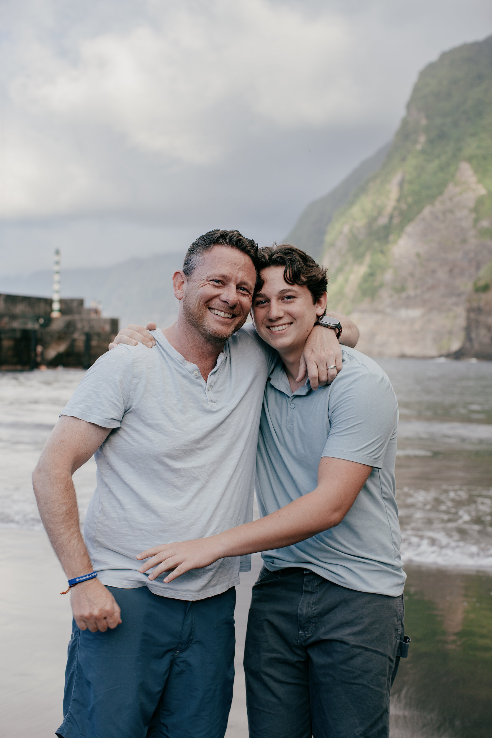 Dad and son laughing cheek to cheek on the dark sand, Seixal Beach, Madeira