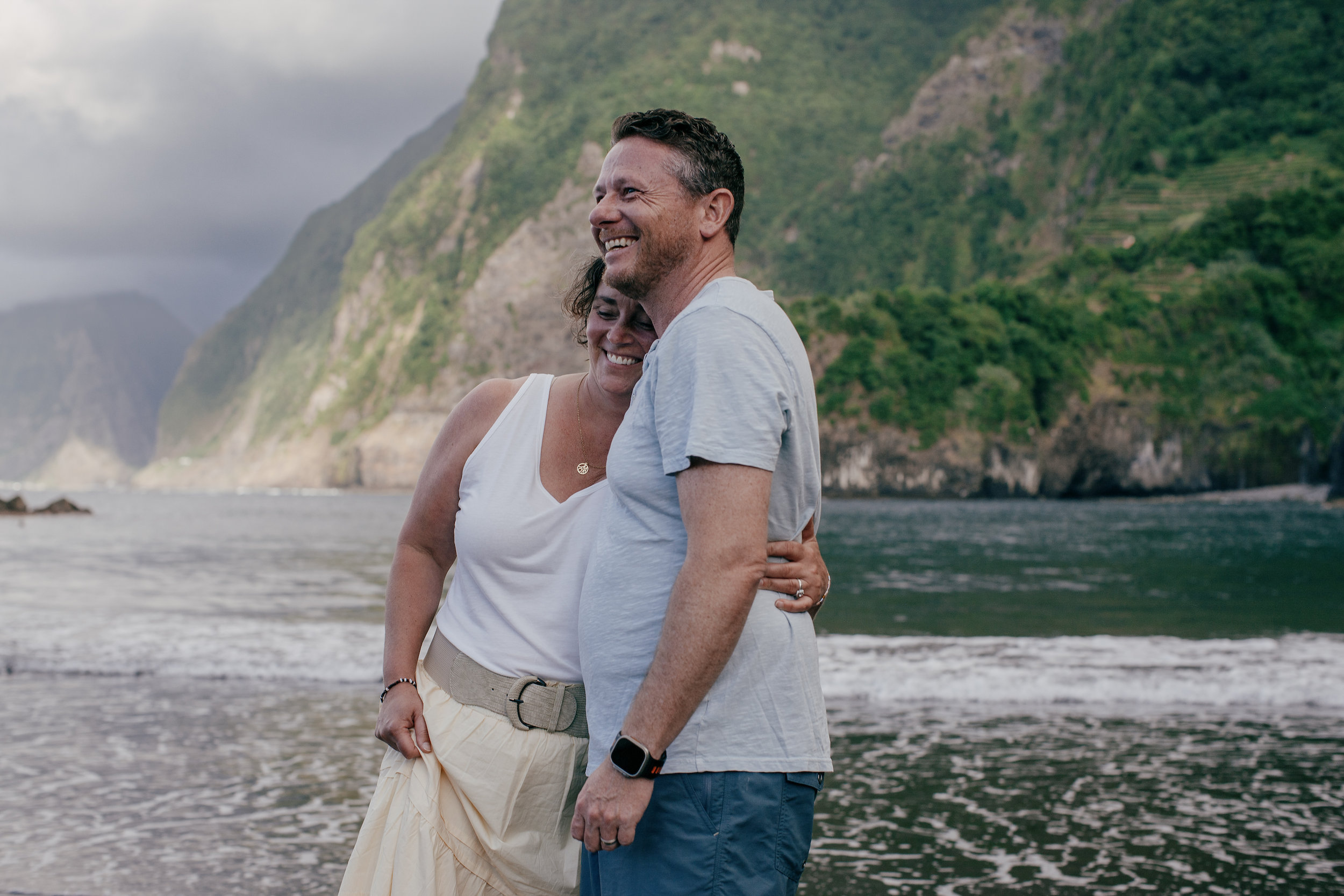Husband and wife hugging with the green cliffs towering behind, Seixal, Madeira