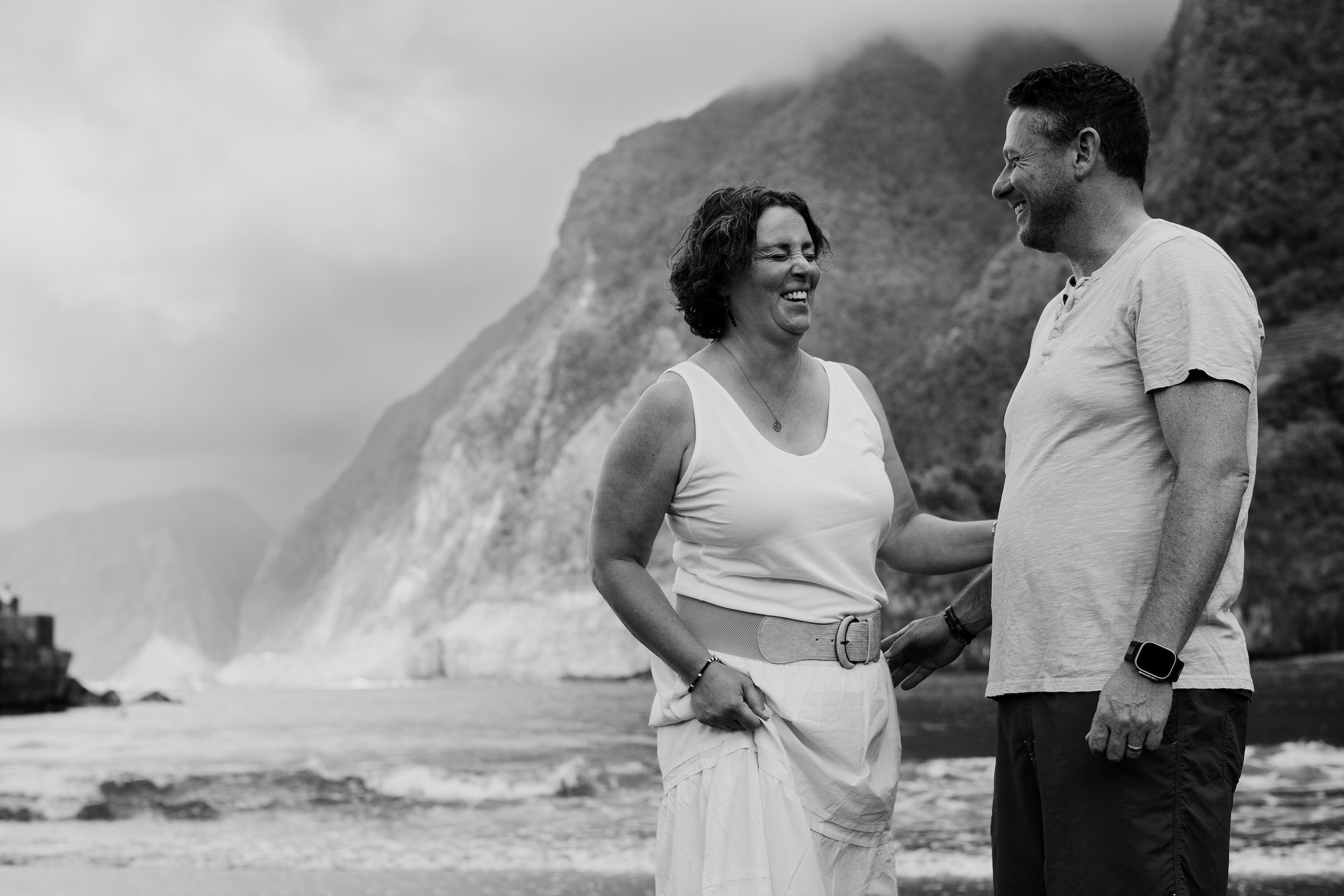 Black and white frame of the couple laughing as surf breaks on the rocks, Seixal, Madeira