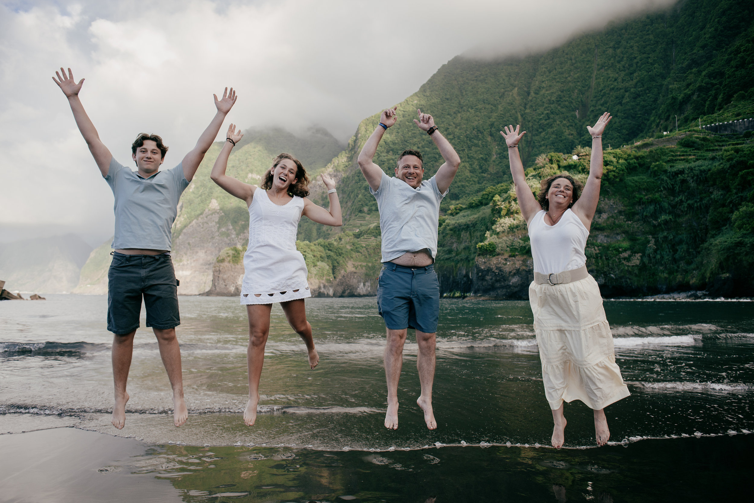 All four jumping at once on the black sand, arms in the air, Seixal Beach, Madeira