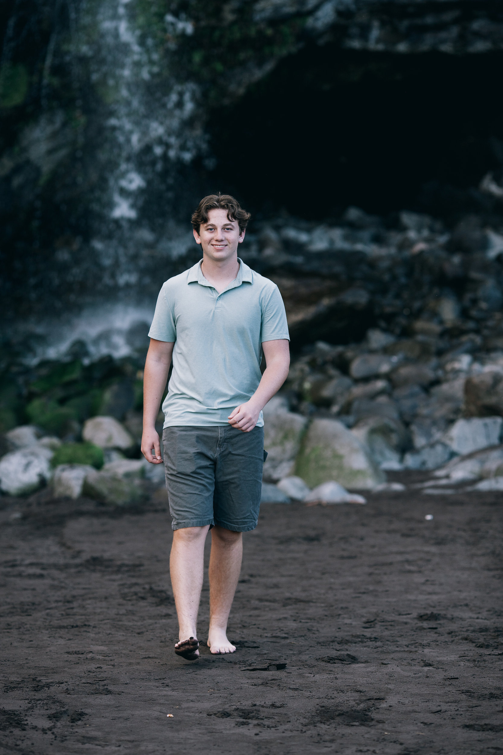 The son in front of the waterfall on the boulders, Seixal, Madeira
