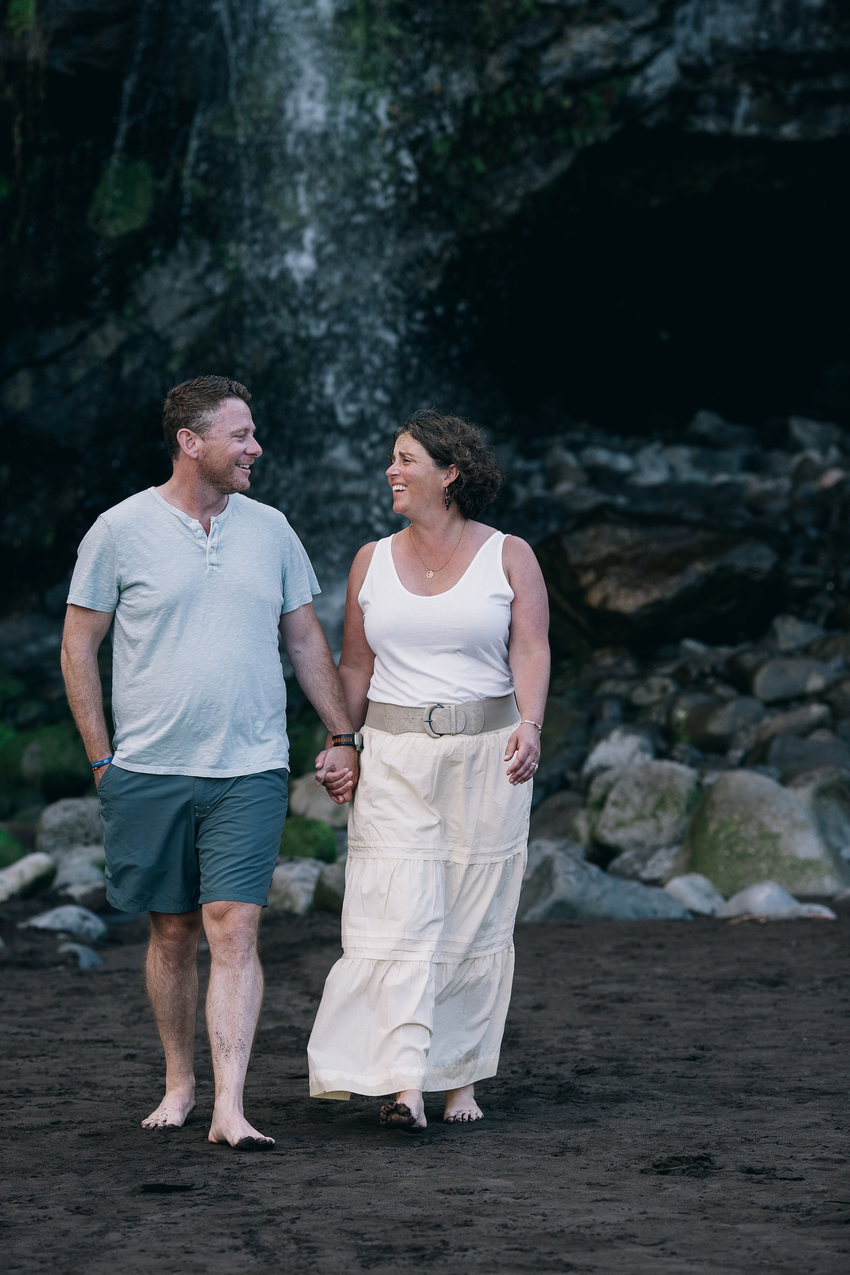 Parents hand in hand under the waterfall cliff, Seixal Beach, Madeira
