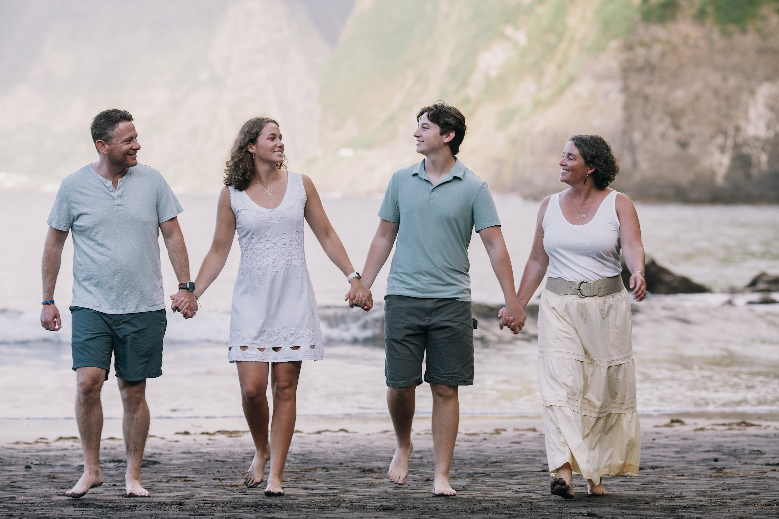 The family walking the black sand holding hands, cliffs soft behind, Seixal, Madeira
