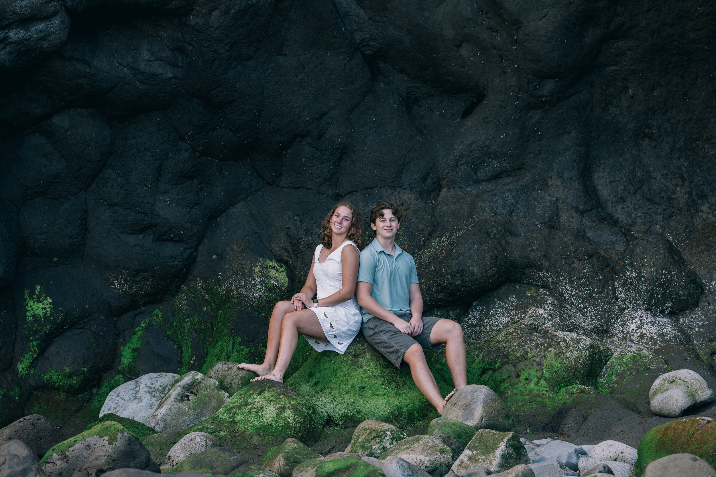 Brother and sister sitting together on the mossy green boulders, Seixal, Madeira