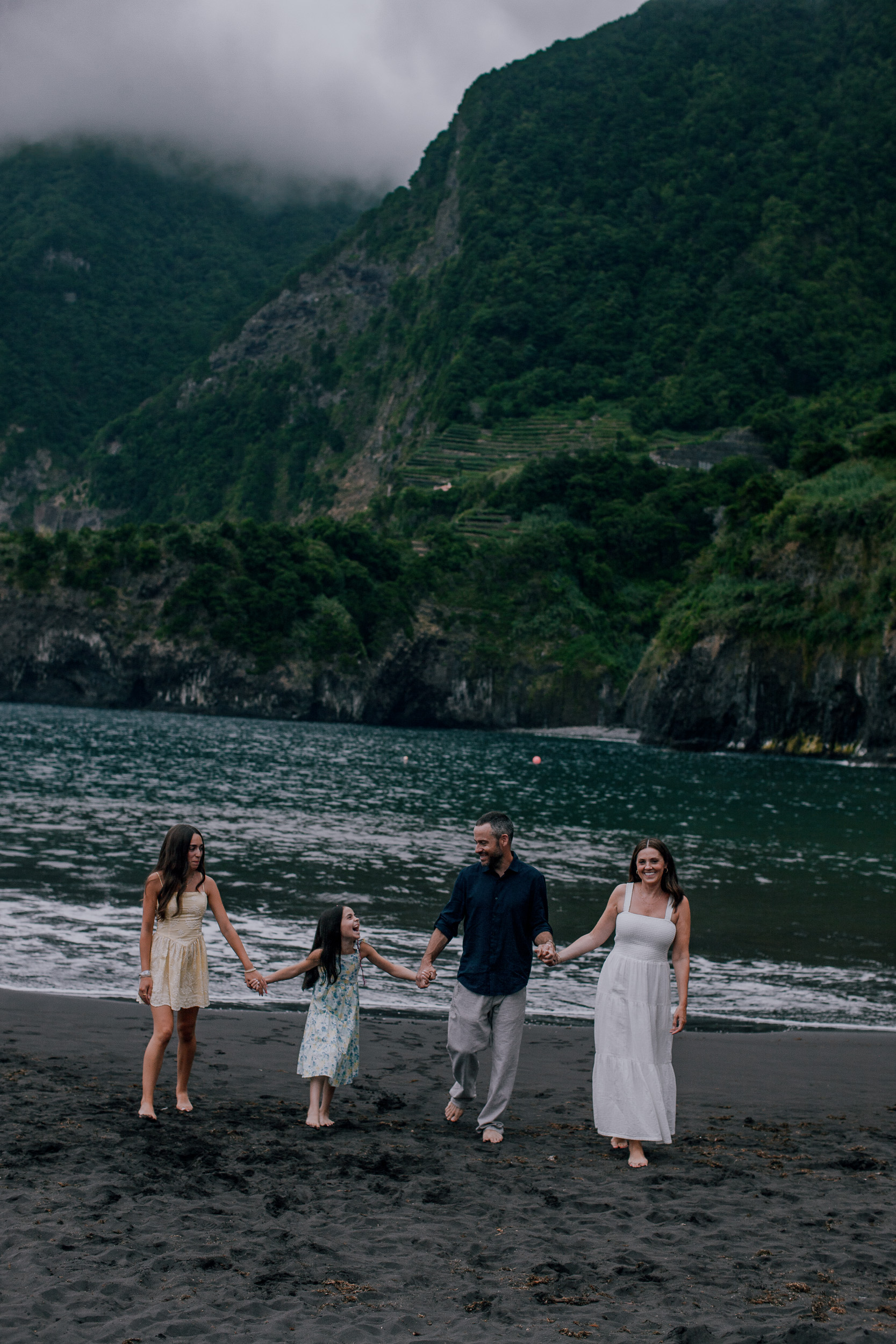 The family in a line at the surf, green cliffs in evening mist behind, Seixal, Madeira