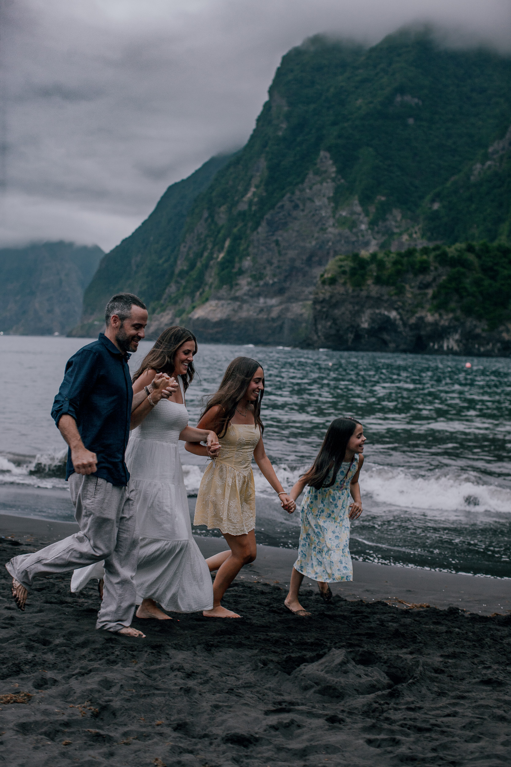 The family mid-run at the surf line on the dark sand, Seixal, Madeira