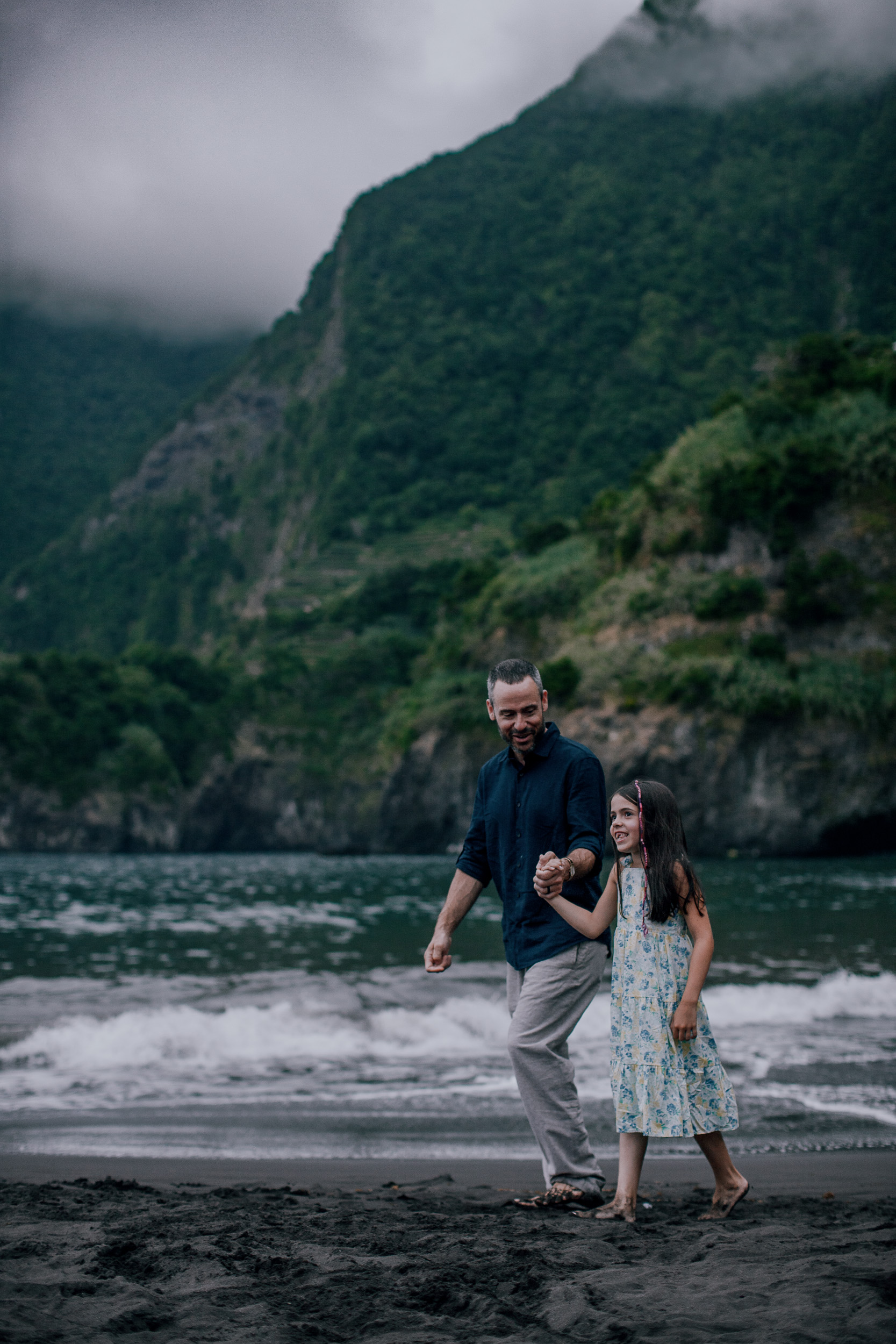 Father and daughter running from a wave laughing, Seixal, Madeira