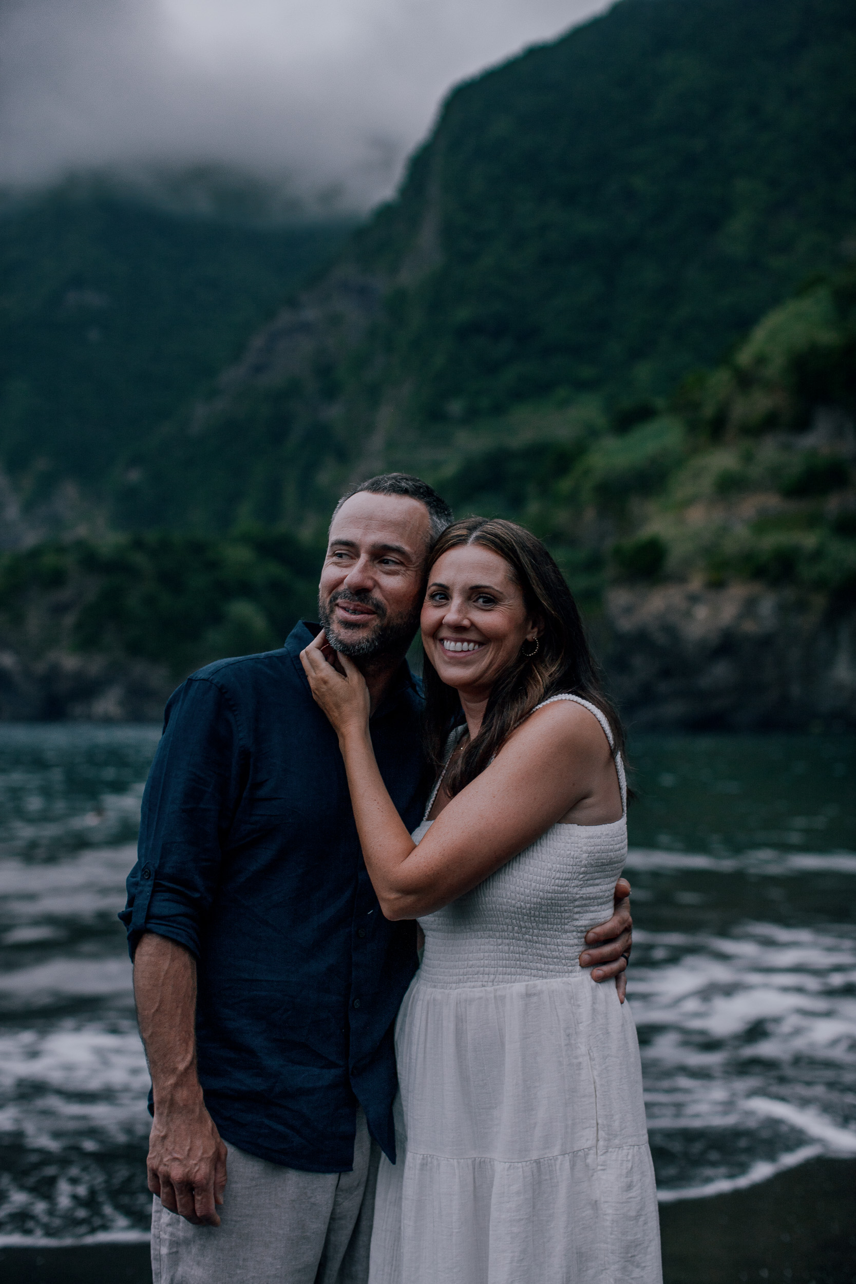 The parents hugging on the black sand, cliffs in cloud behind, Seixal, Madeira