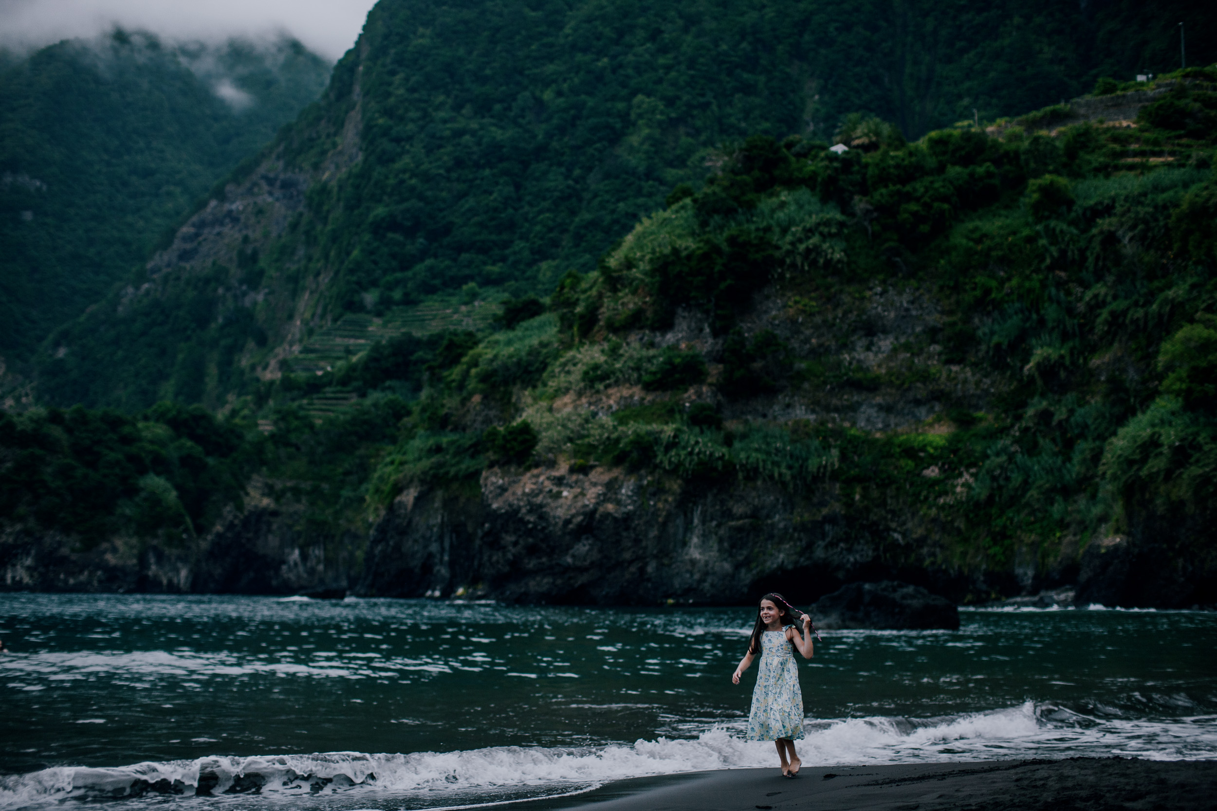 Small figure of the daughter at the surf under the green wall, Seixal, Madeira