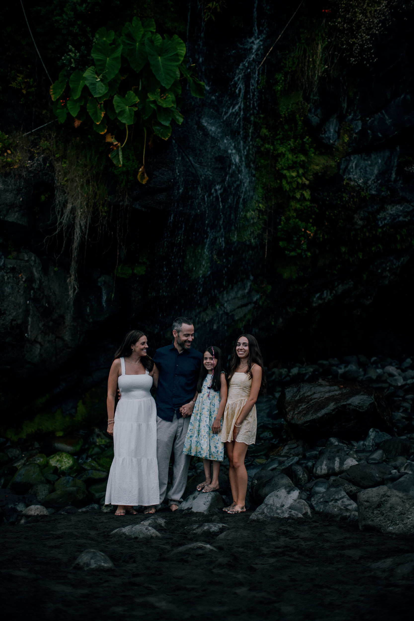 The family under the dark cliff by the waterfall, Seixal Beach, Madeira