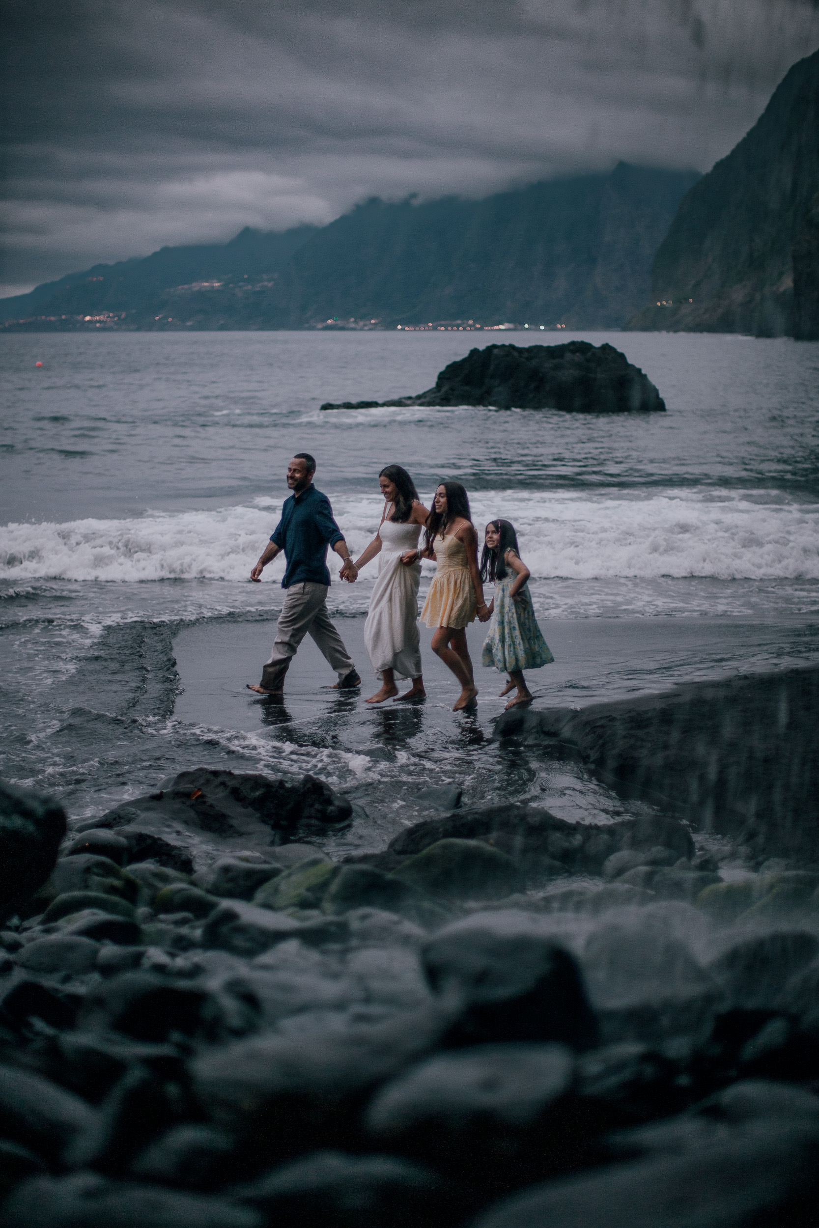 Family crossing the dark water together, cliffs dim behind, Seixal, Madeira