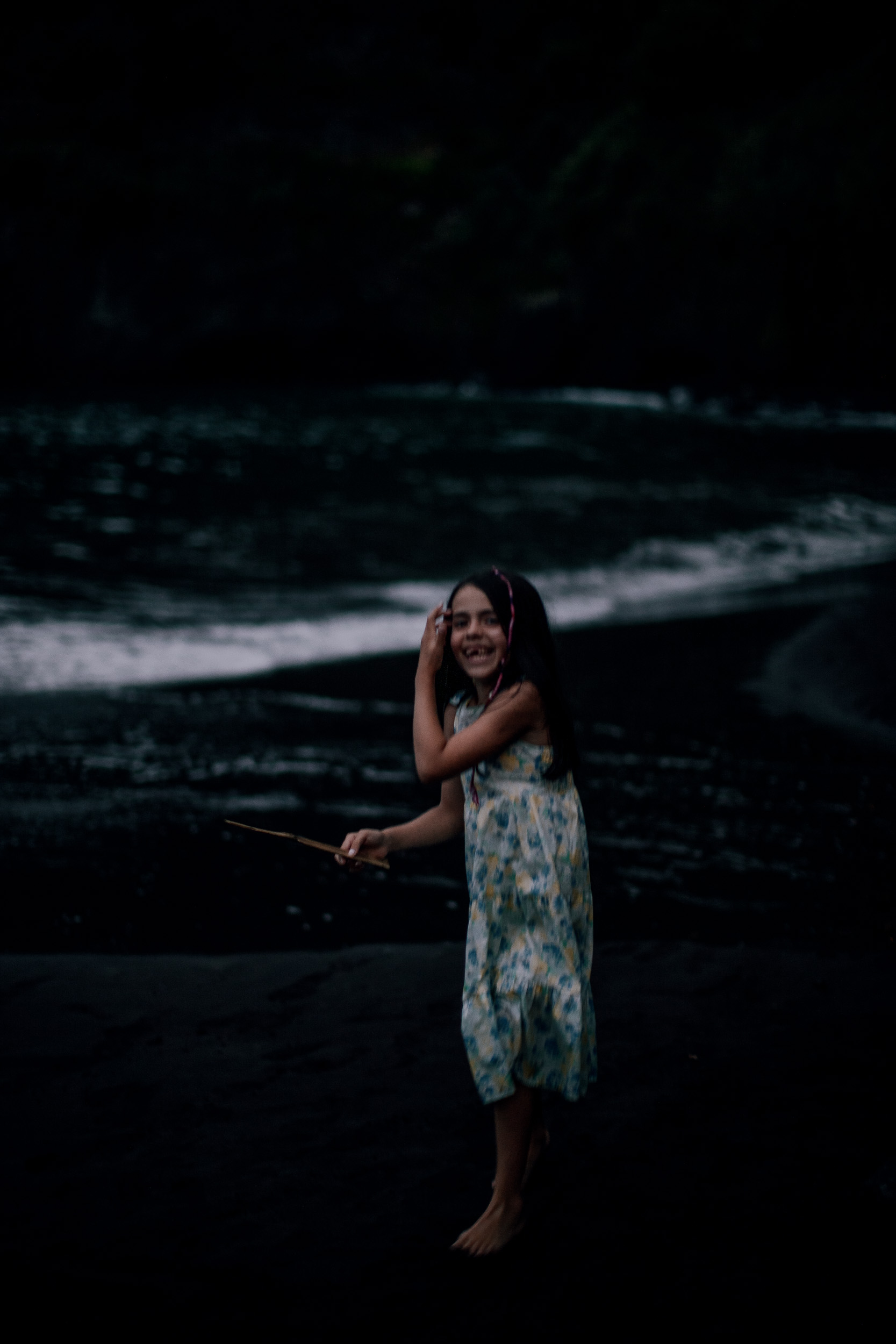 The girl brushing hair from her face at the water, dusk at Seixal, Madeira