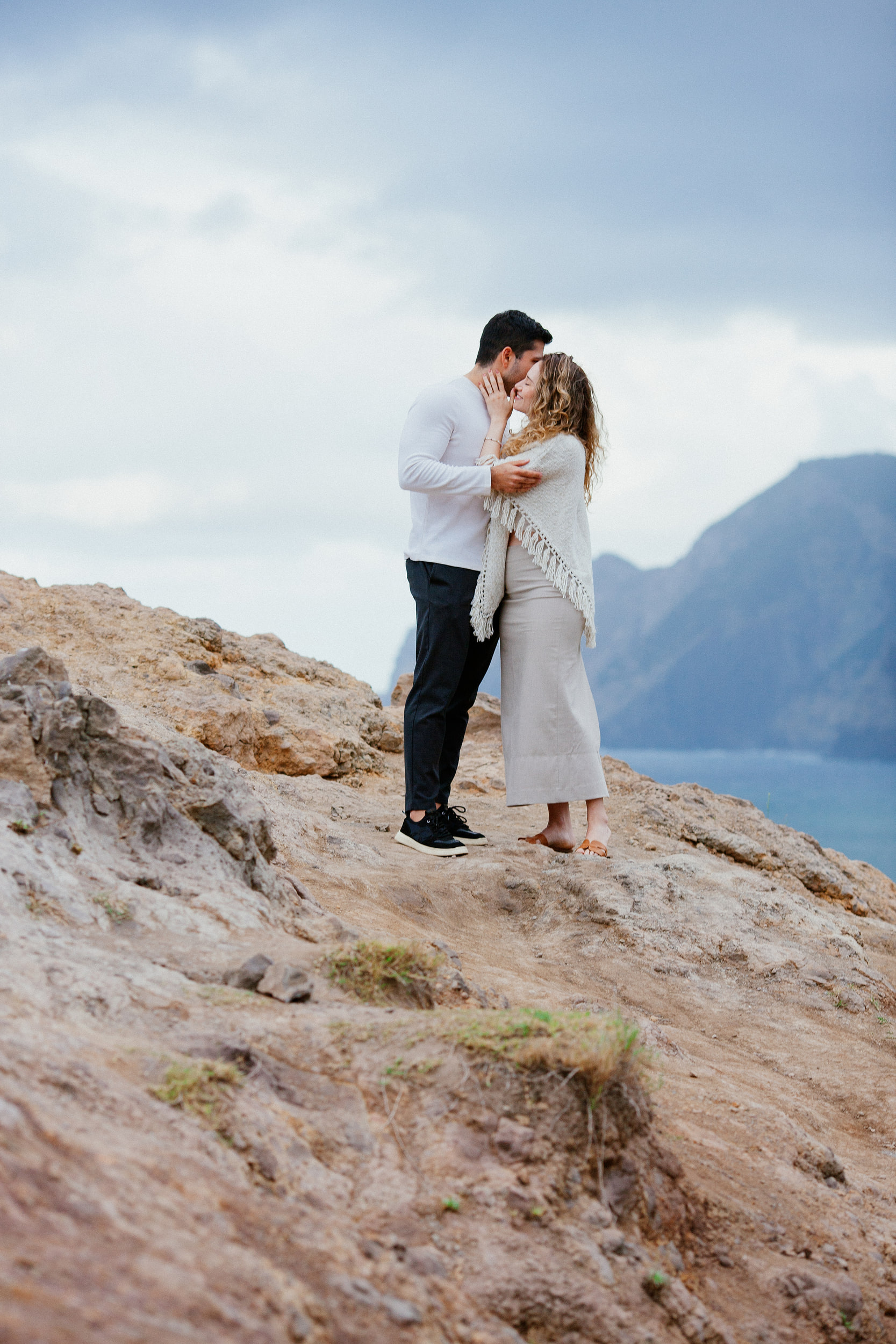 Lucas and Isabela kissing on the rocks, mountains and sea cliffs behind, Miradouro do Guindaste, Madeira