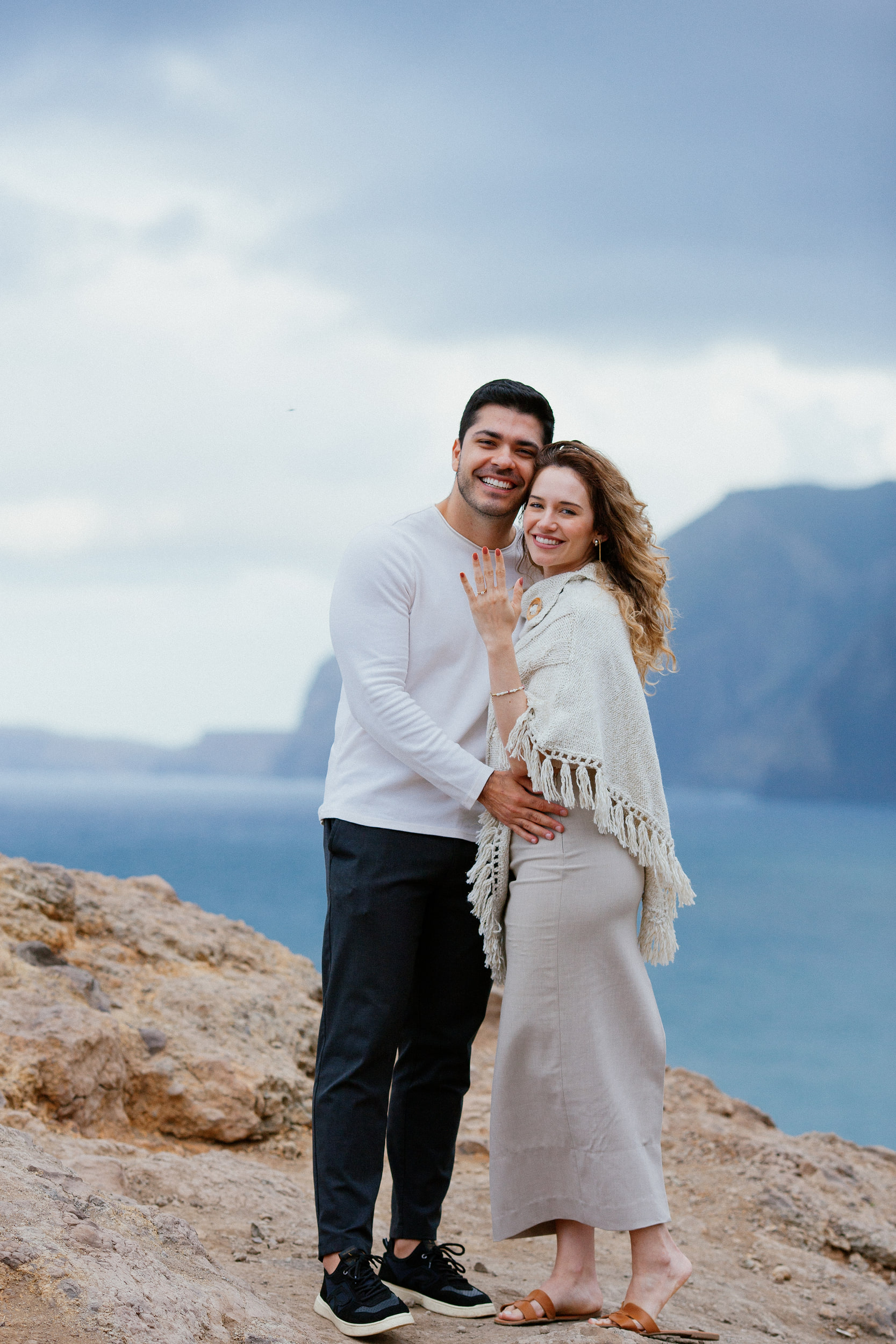 Lucas and Isabela smiling at the camera, Isabela showing her ring hand, cliffs behind, Miradouro do Guindaste, Madeira