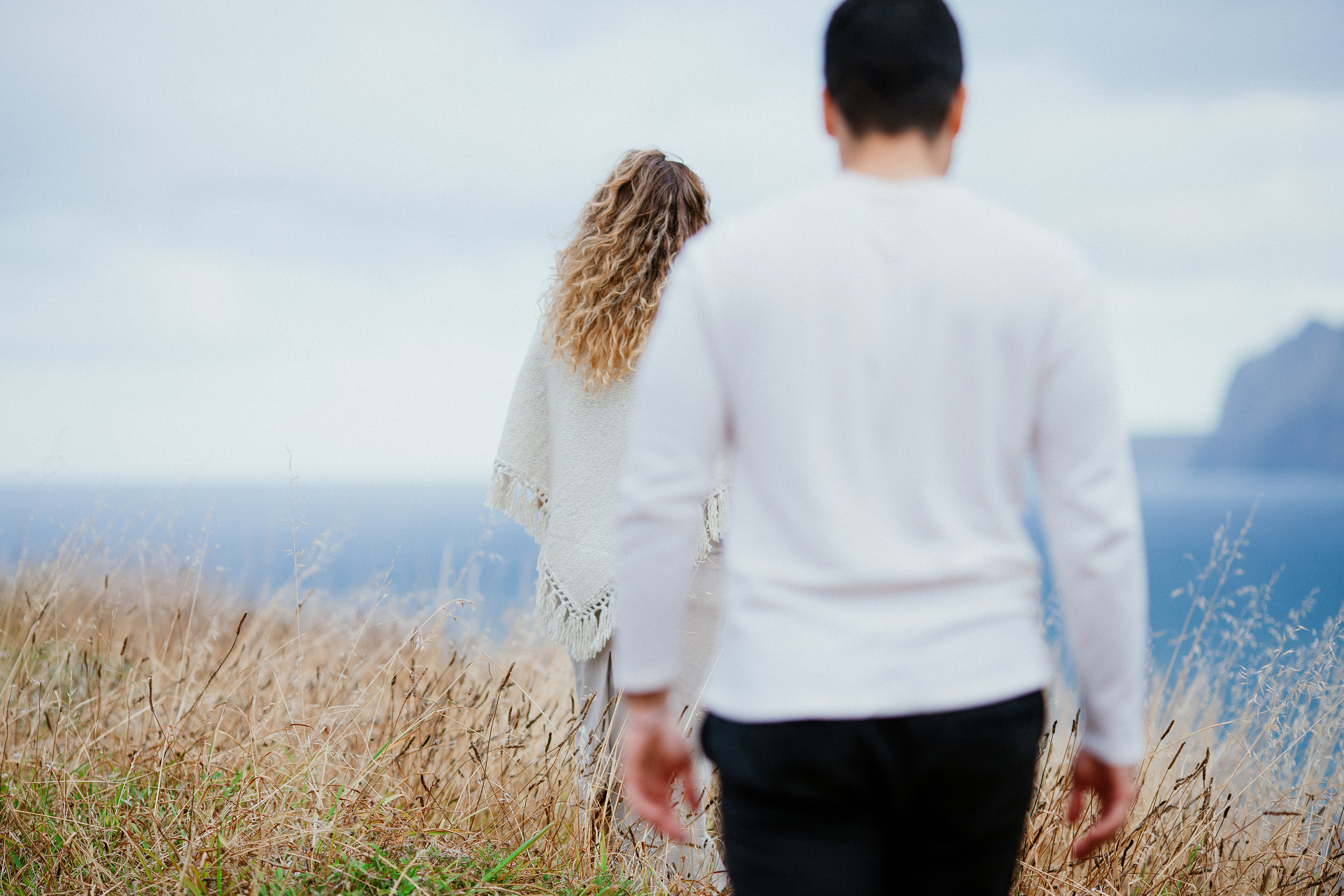 Lucas following Isabela through the tall grass toward the sea, Miradouro do Guindaste, Madeira